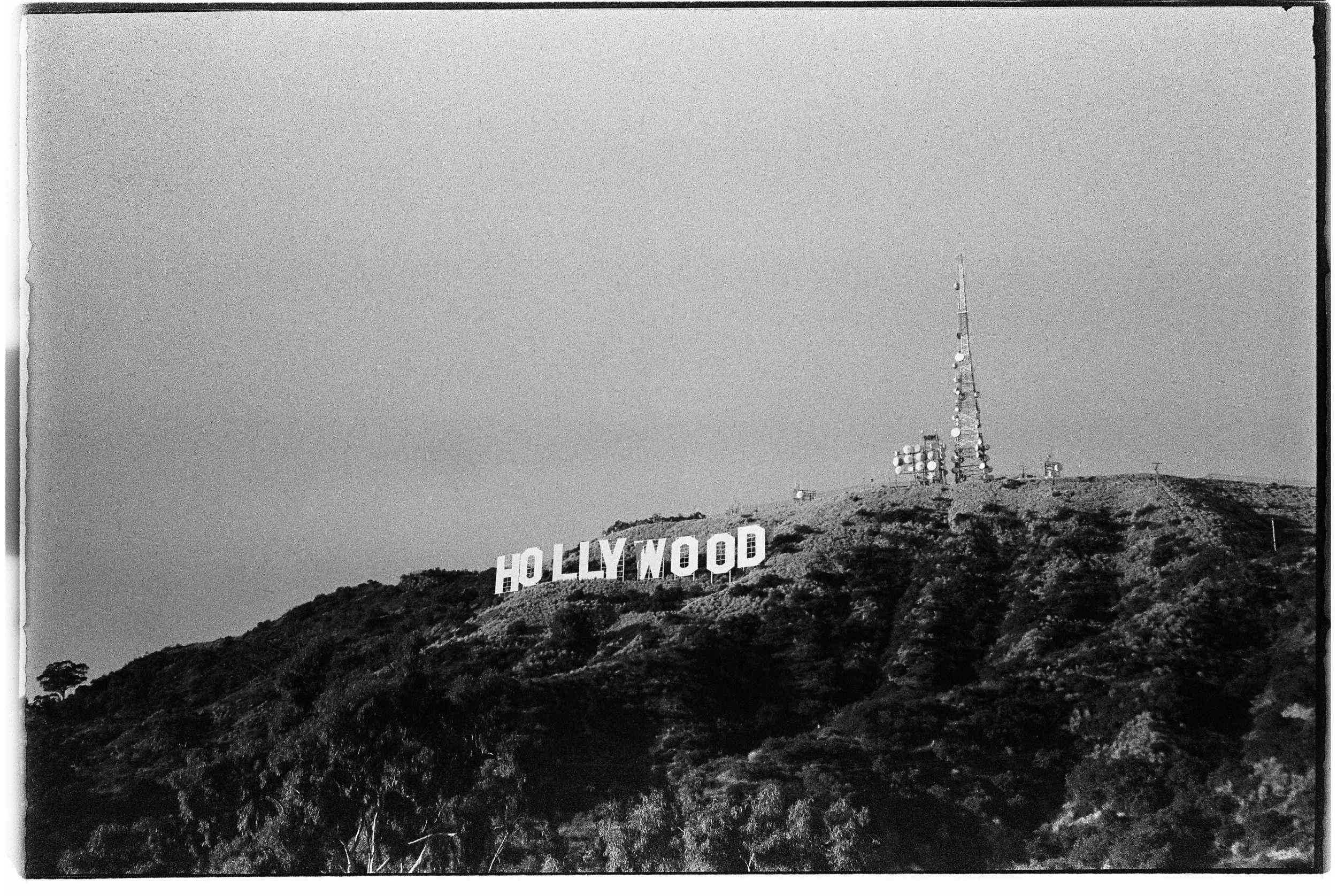 Black and white photo of the Hollywood sign on a hillside with trees and communication towers.