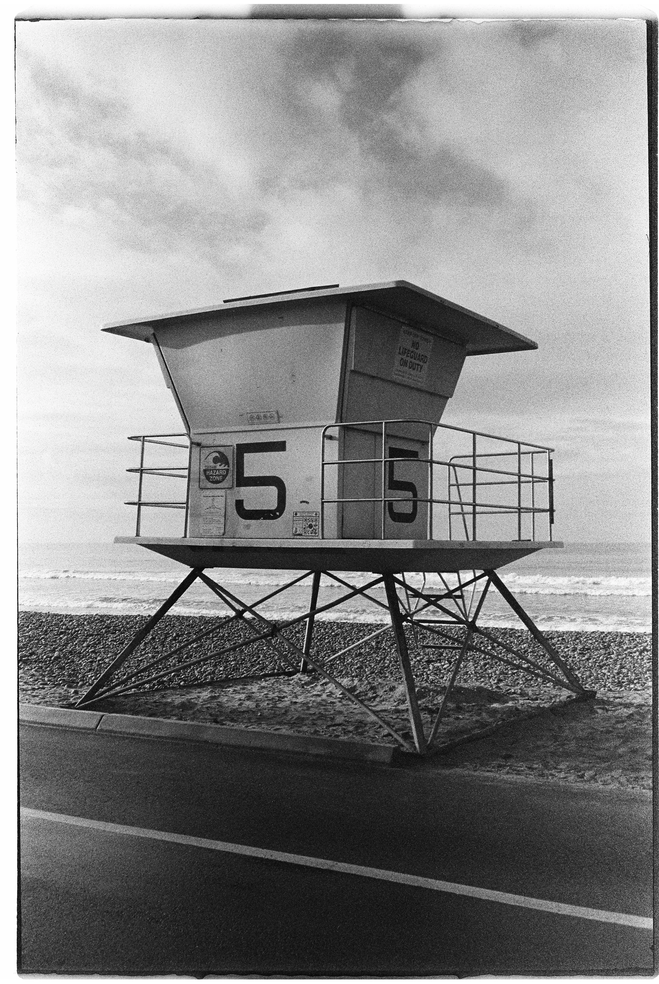 A vintage lifeguard tower with the number 5, situated on a pebble beach near the ocean, with a partly cloudy sky overhead.