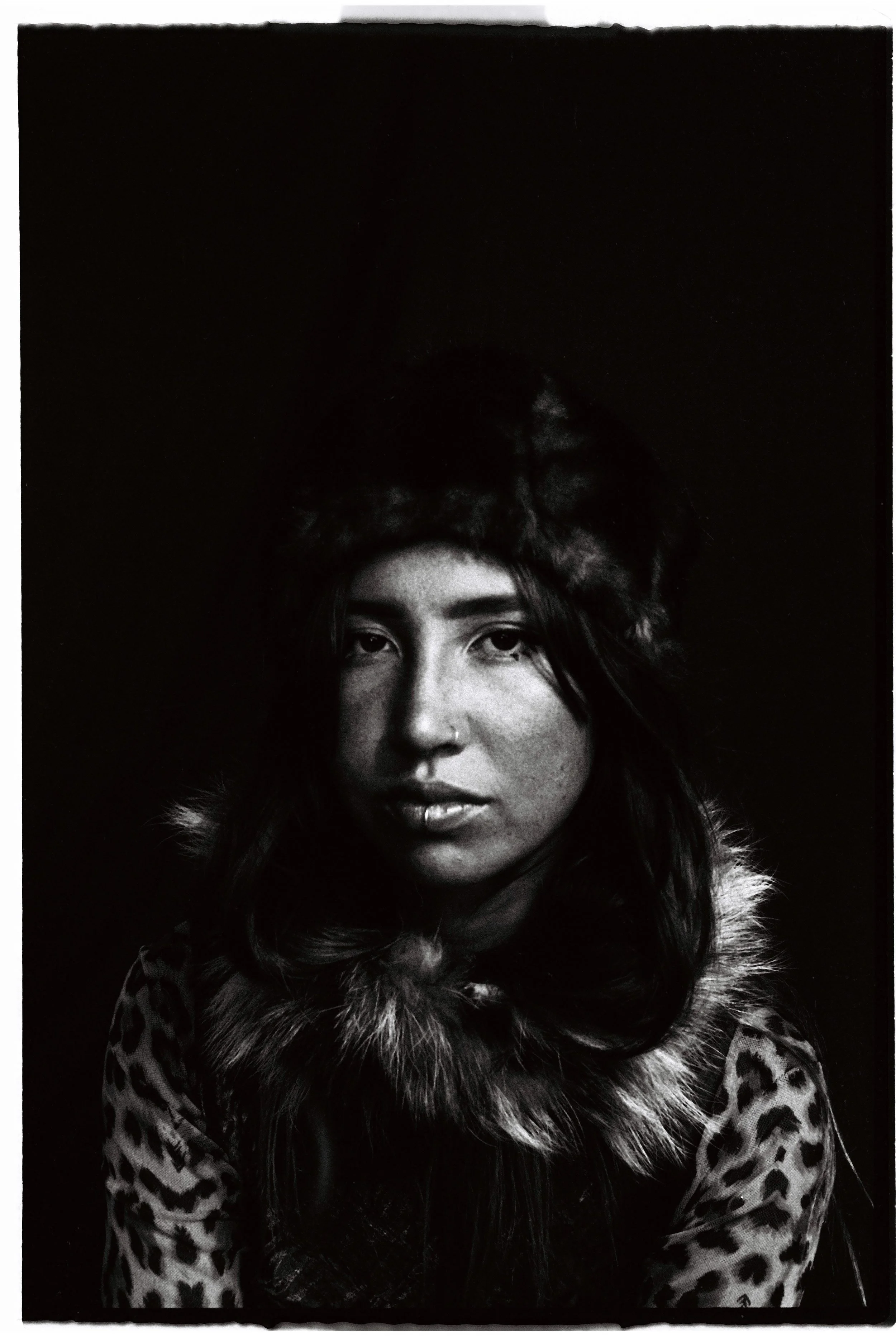 Black-and-white portrait of a woman wearing a furry hat and leopard print coat, looking directly at the camera.