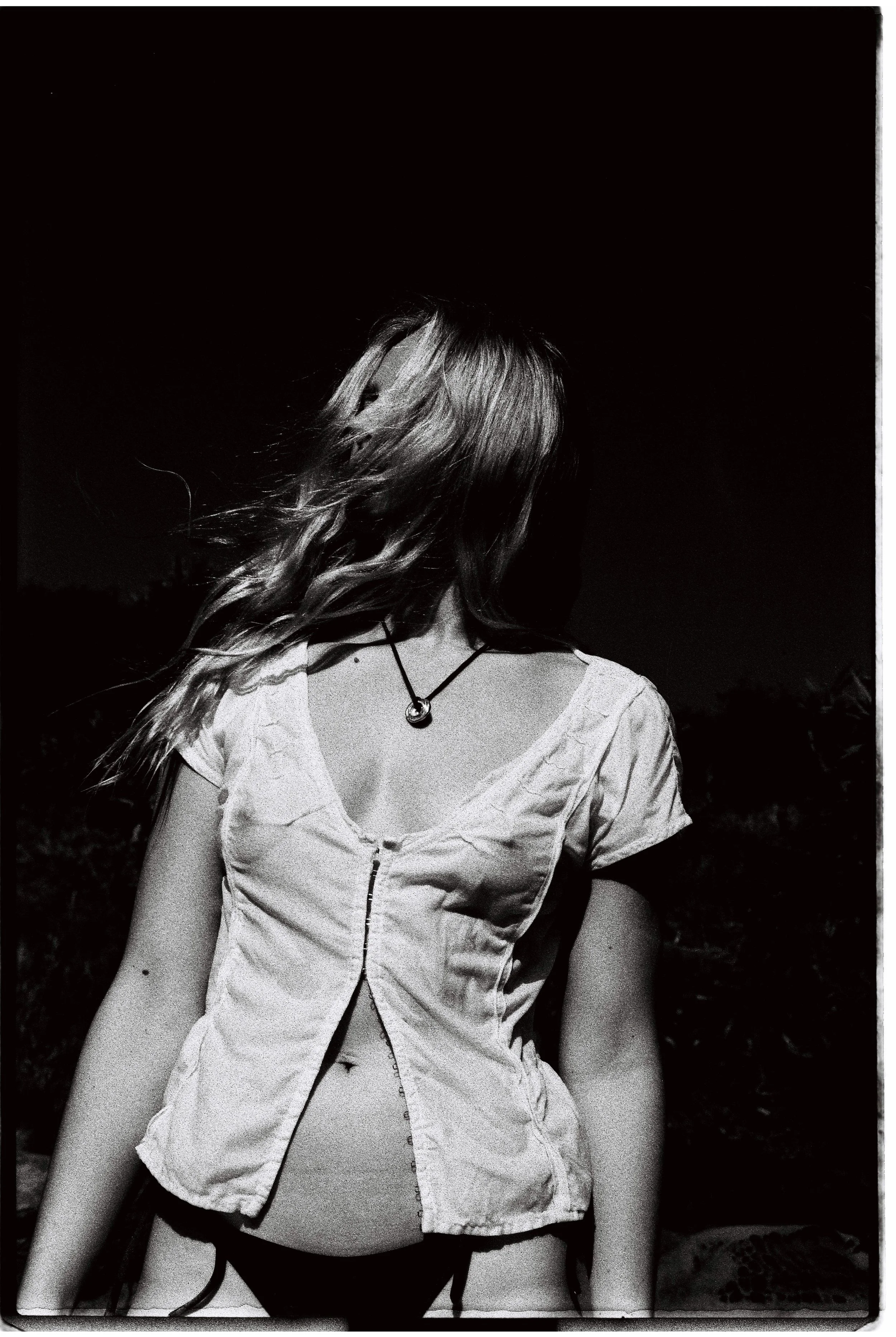 A woman with wavy hair wearing a short-sleeved blouse with a zipper and a necklace, standing outdoors at night.