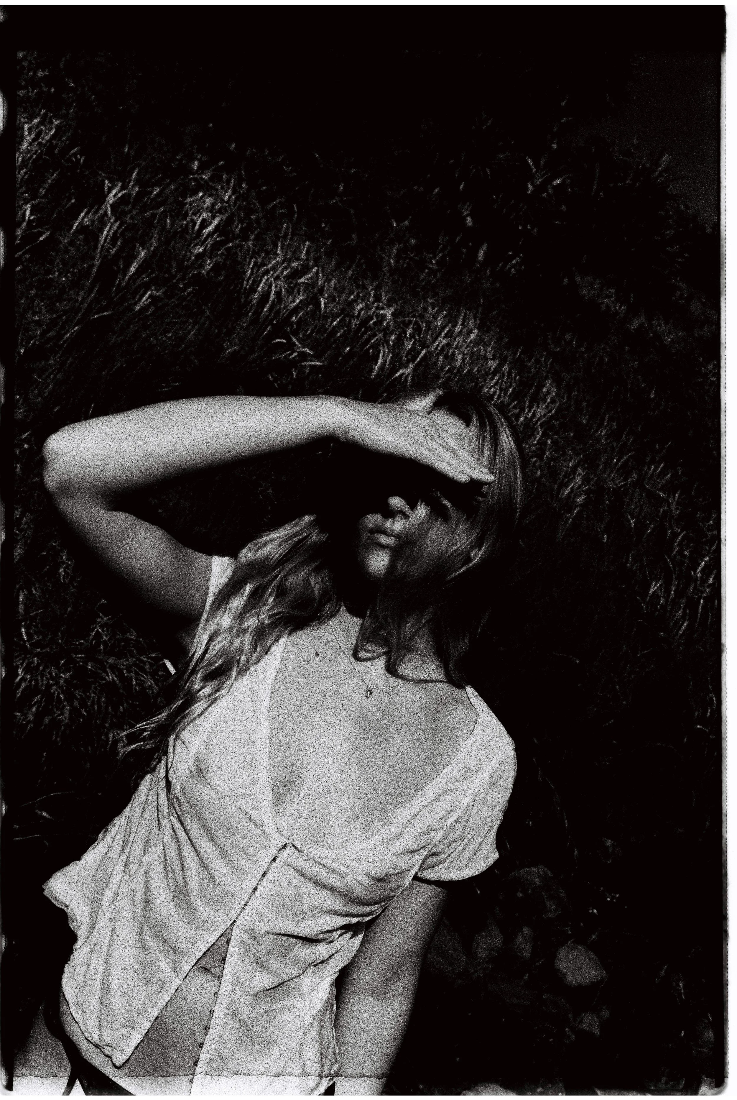 A woman lying on grass with her hand shielding her eyes from the sunlight.