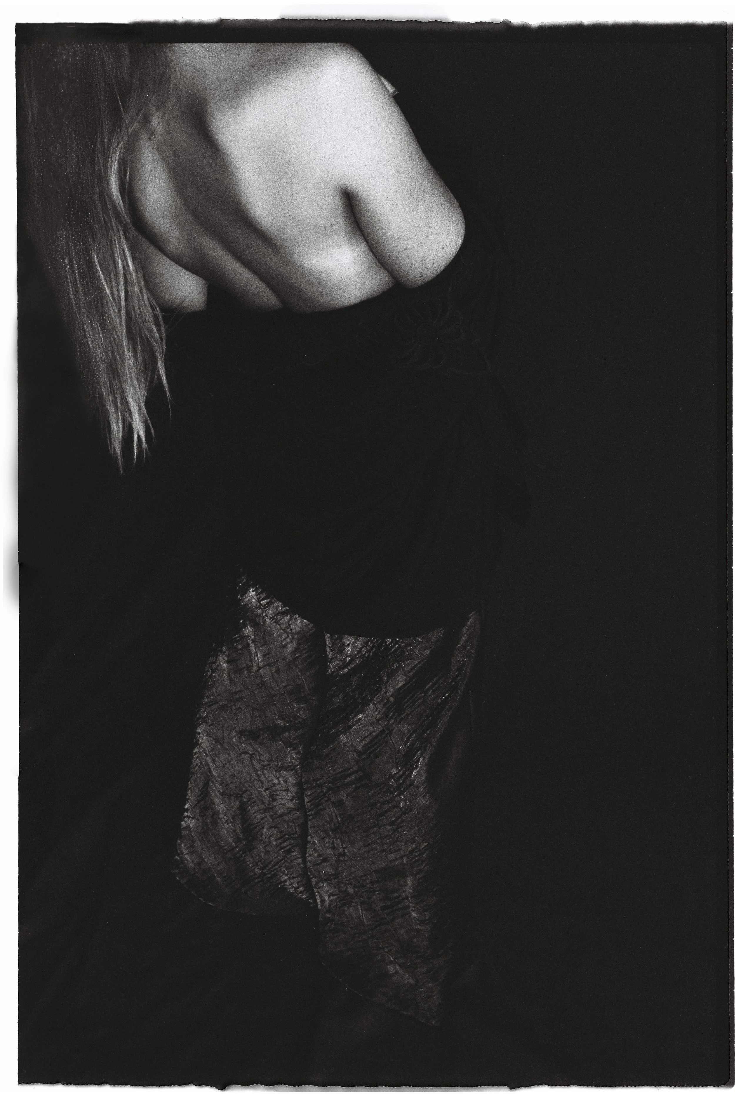 Close-up black and white photo of a person's shoulder, part of their chest, and their hair, with a fabric or dress that has a textured pattern.