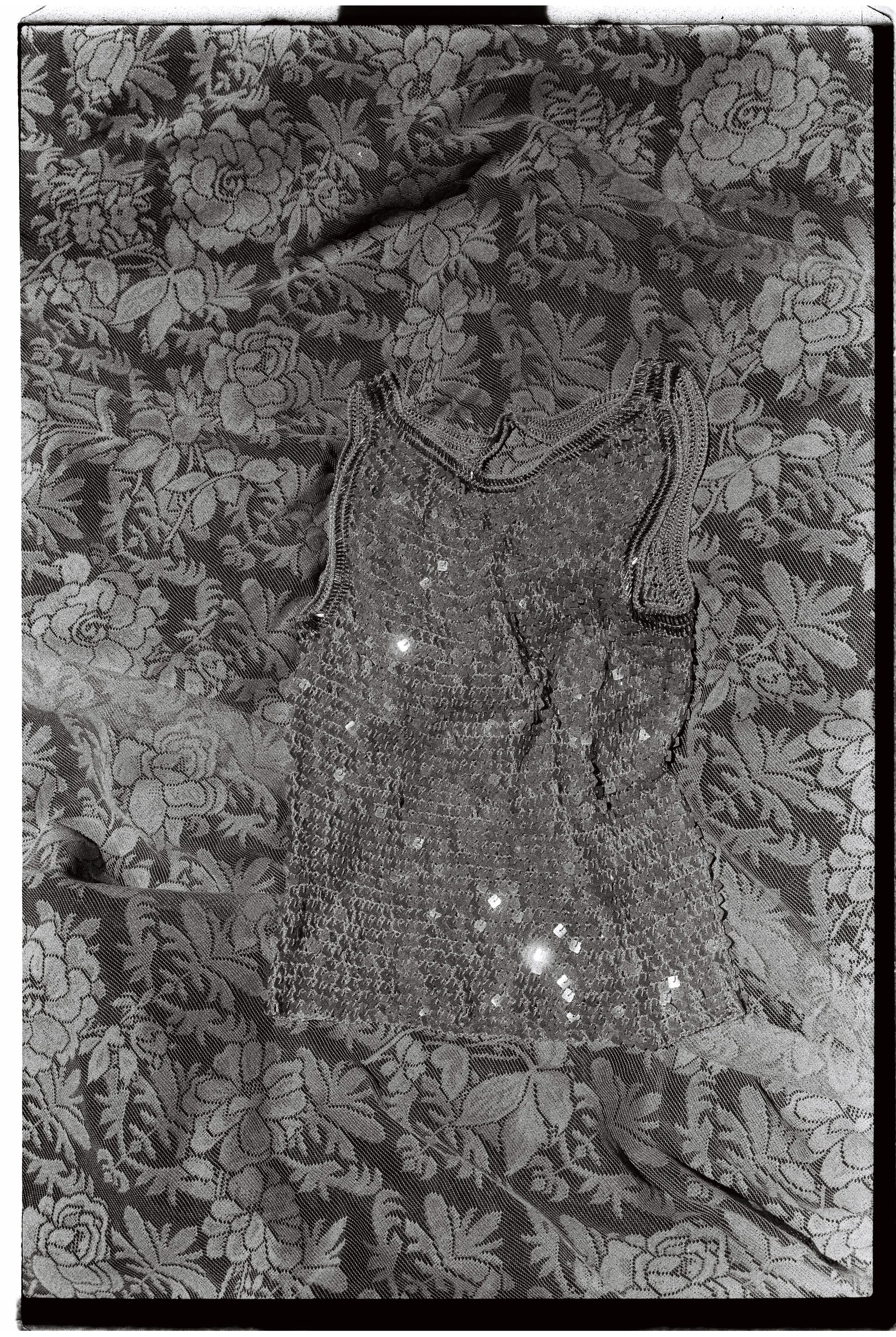 A dress made of shiny sequins laid on a floral patterned fabric surface.