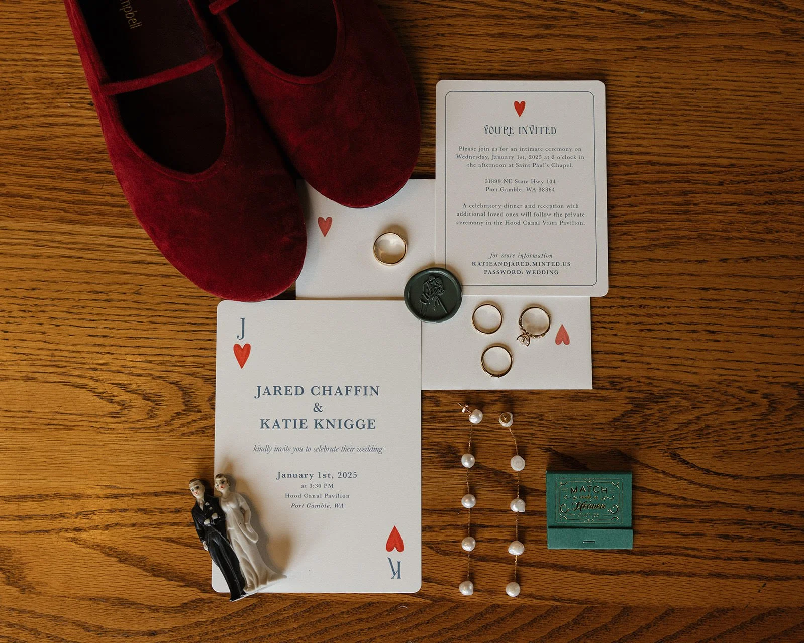 Wedding invitation suite with shoes, jewelry, and small figurines on a wooden surface.