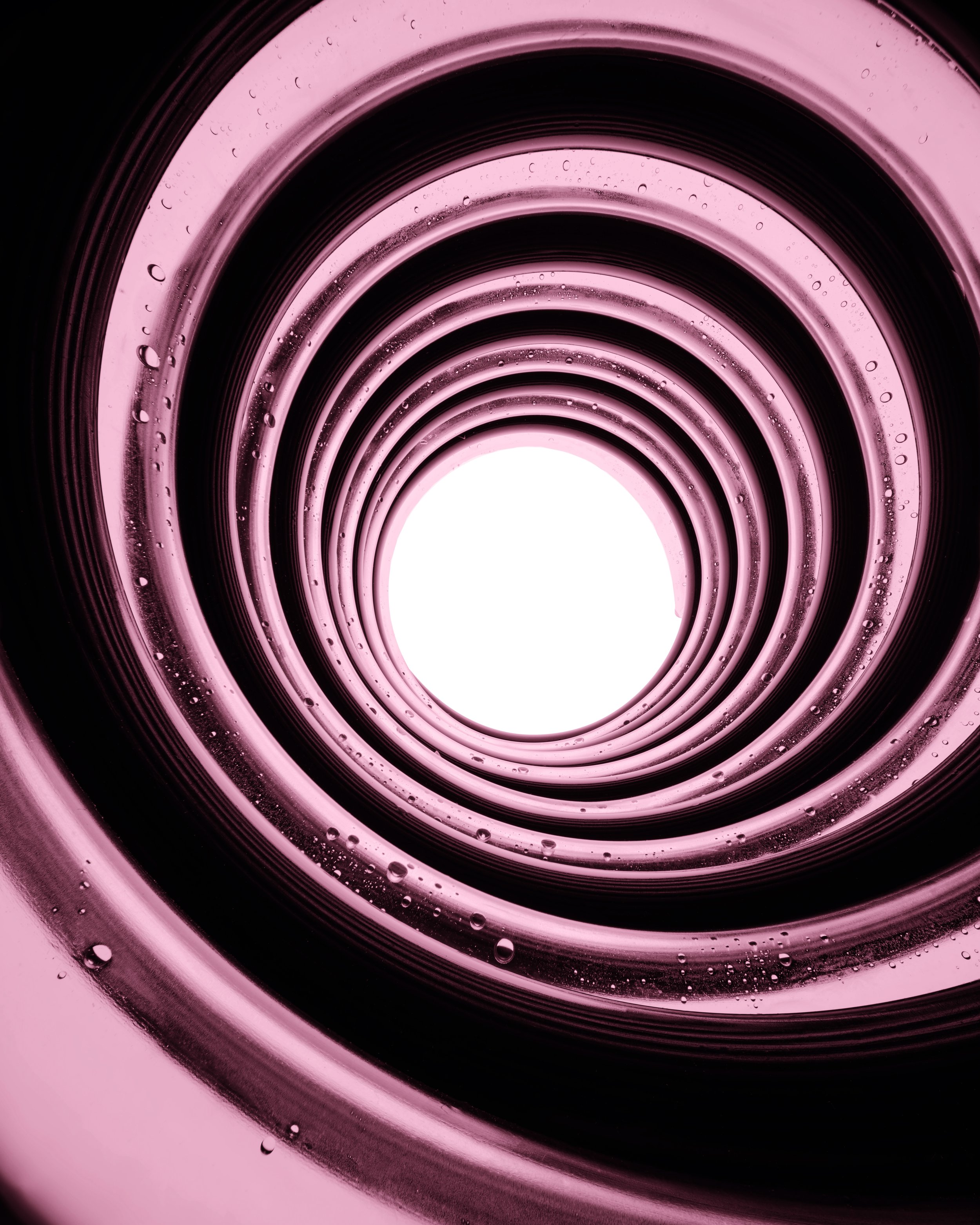 Close-up of a spiral pattern with pink and black concentric circles and water droplets on the surface.