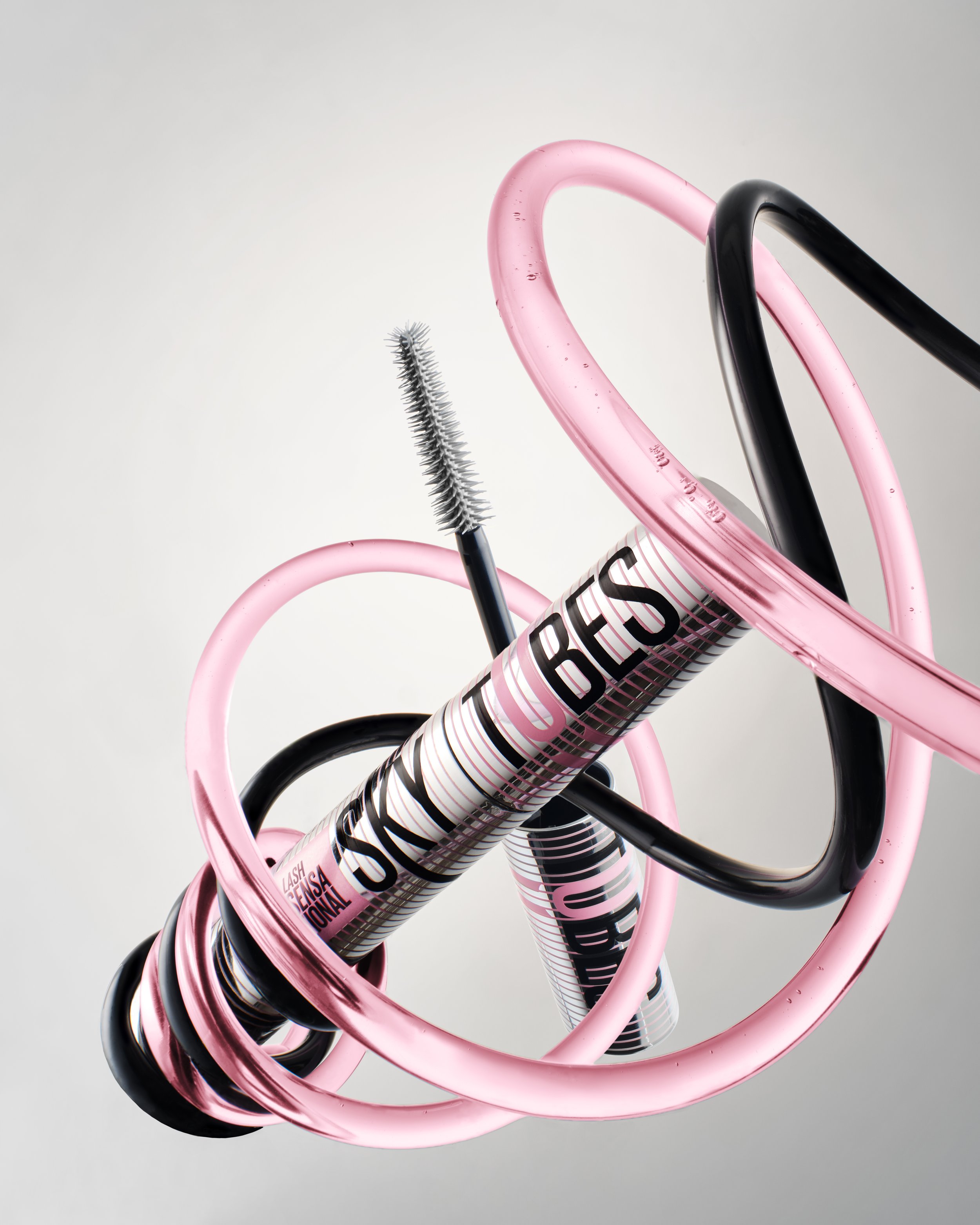 Close-up image of intertwined pink and black hoses or tubes against a neutral background, with one black brush-like object visible.