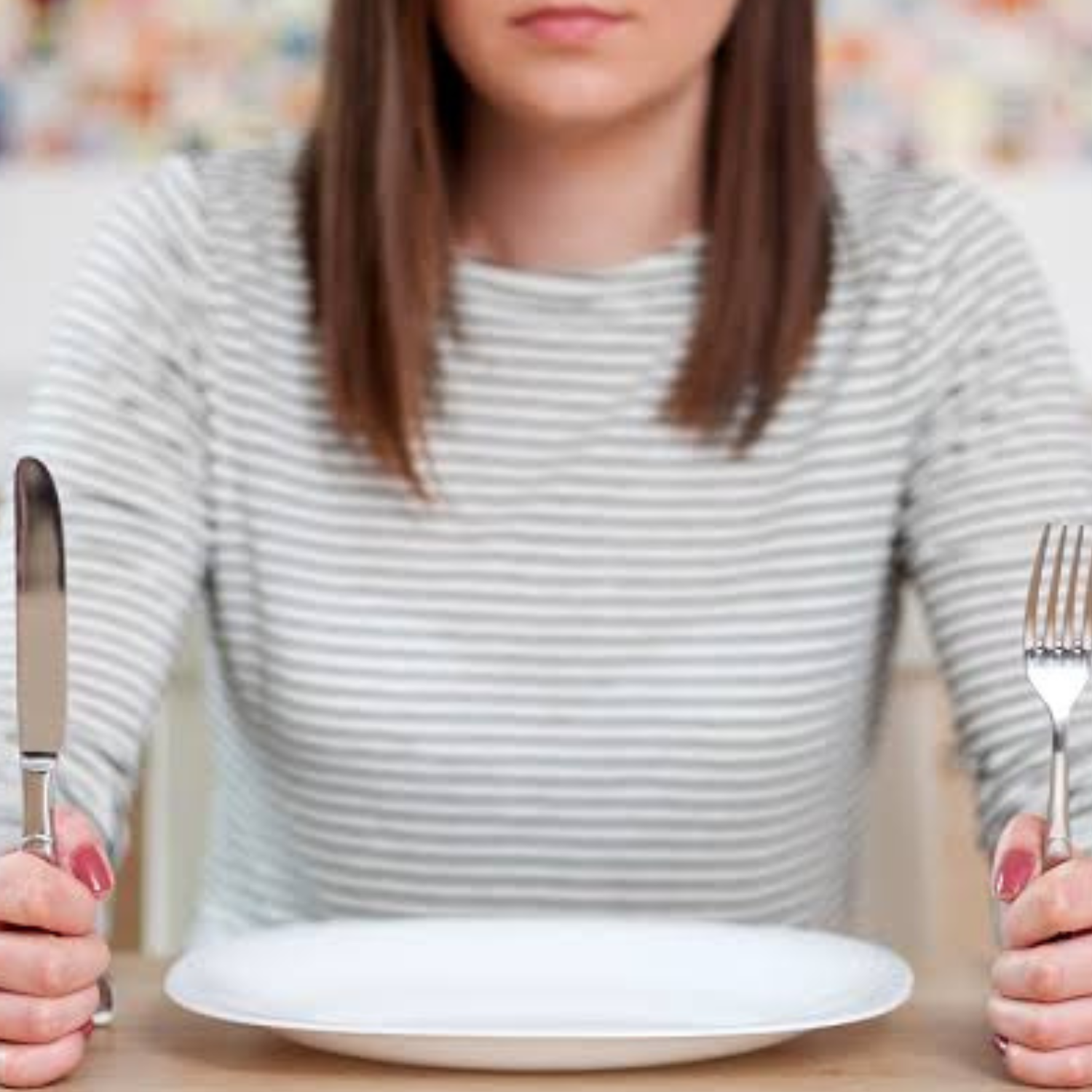 Woman sitting at table in front of an empty plate holding a fork and a knife