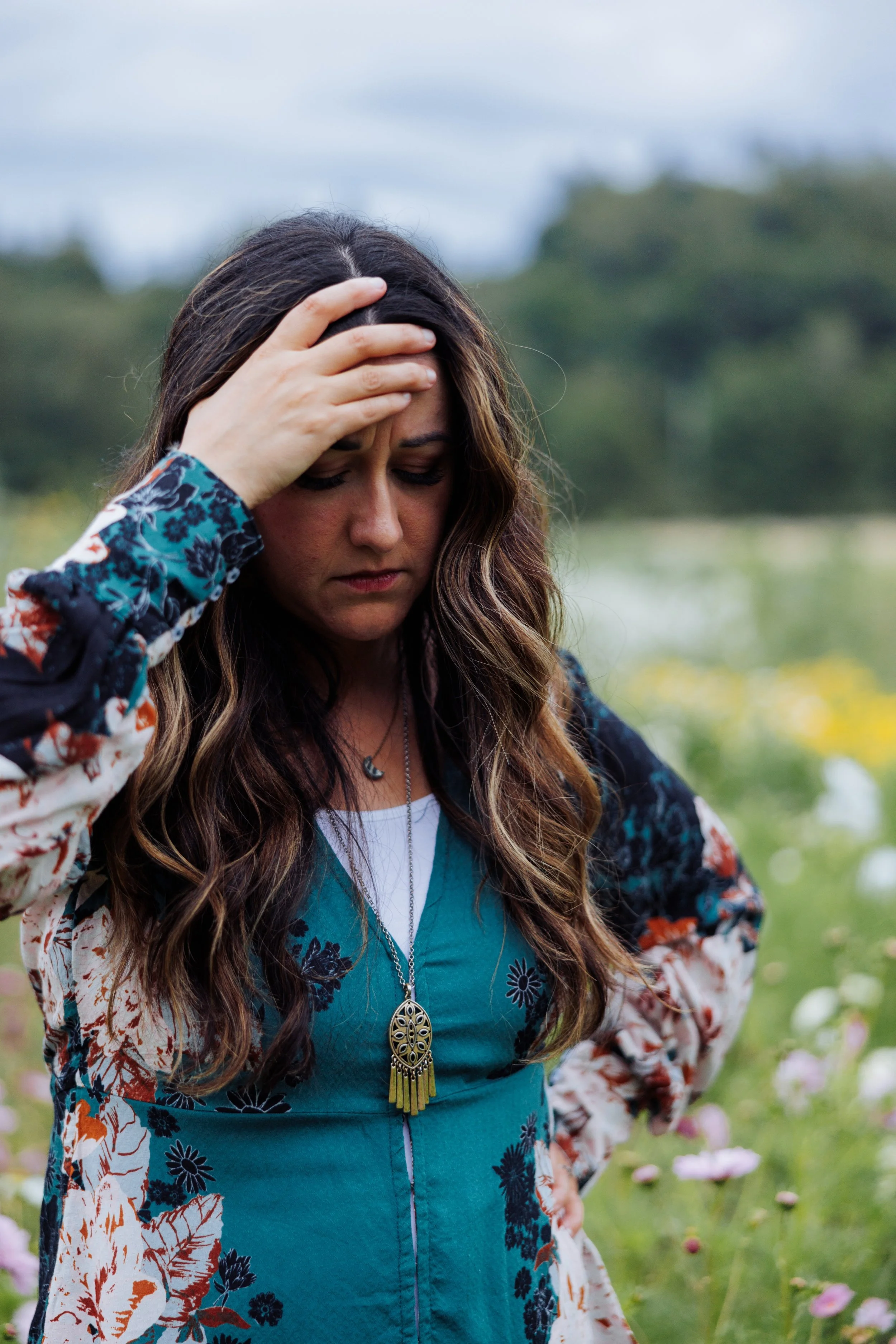 Woman standing in field with hand on forehead, distressed.