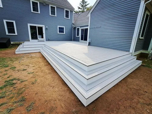 Backyard with a newly built white wooden deck attached to a blue house with multiple windows and sliding doors.