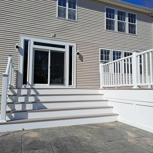 Backyard with white deck stairs, sliding glass door, beige siding house, and multiple windows.
