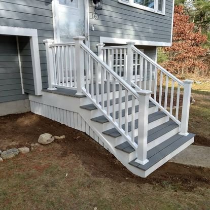 Exterior view of a gray house with a staircase leading to the front door, featuring white railings and steps.