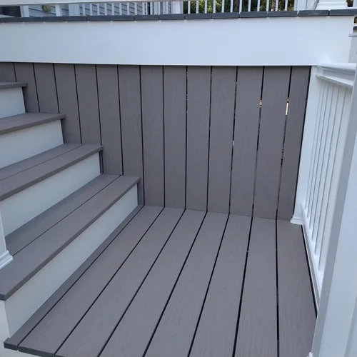 A small outdoor deck with stairs, featuring gray wooden flooring, matching gray wooden wall, and white railings.