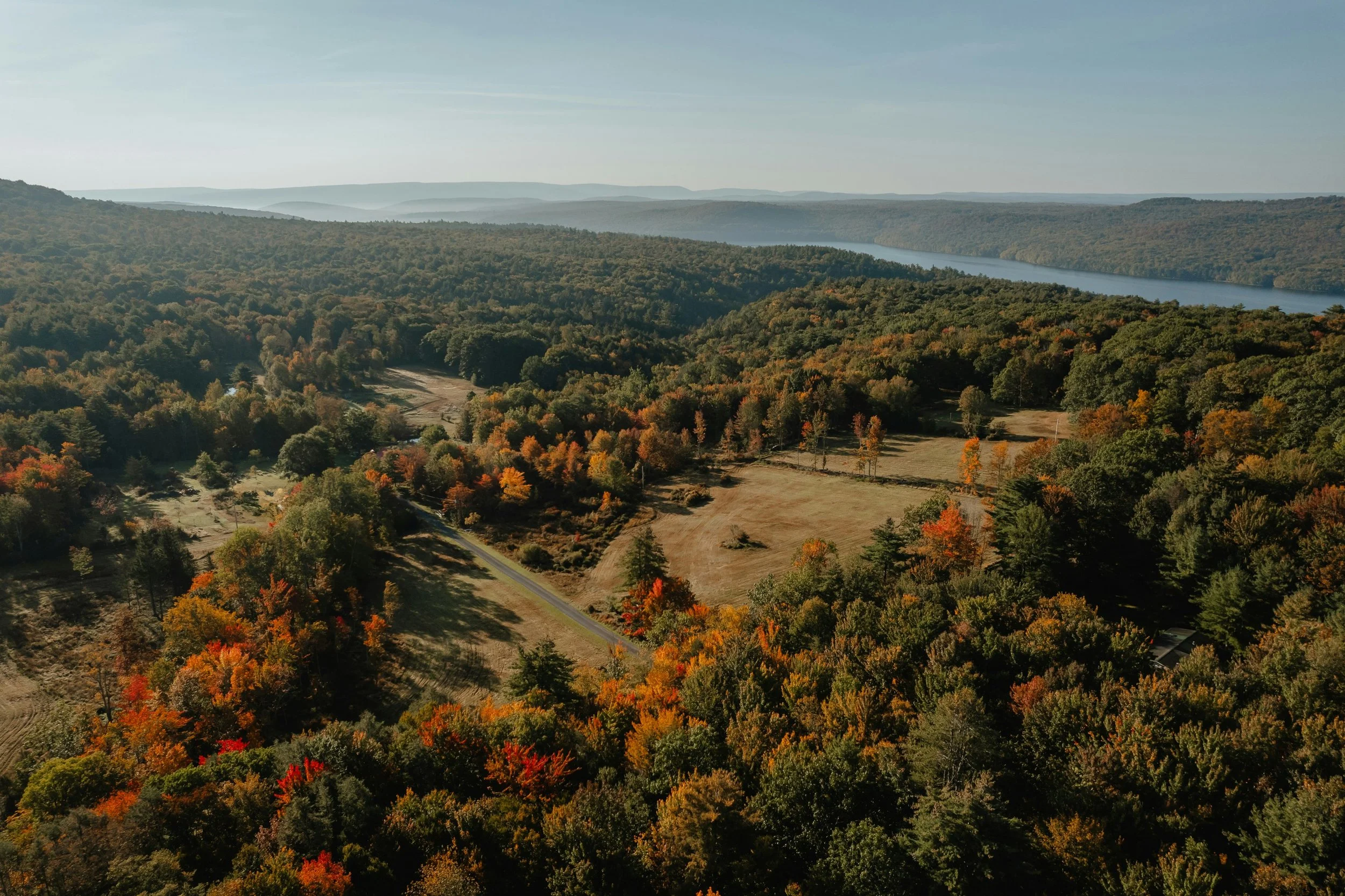 Aerial view of a scenic landscape with a river flowing through a forested valley during autumn, showing trees with fall foliage and mountains in the distance.
