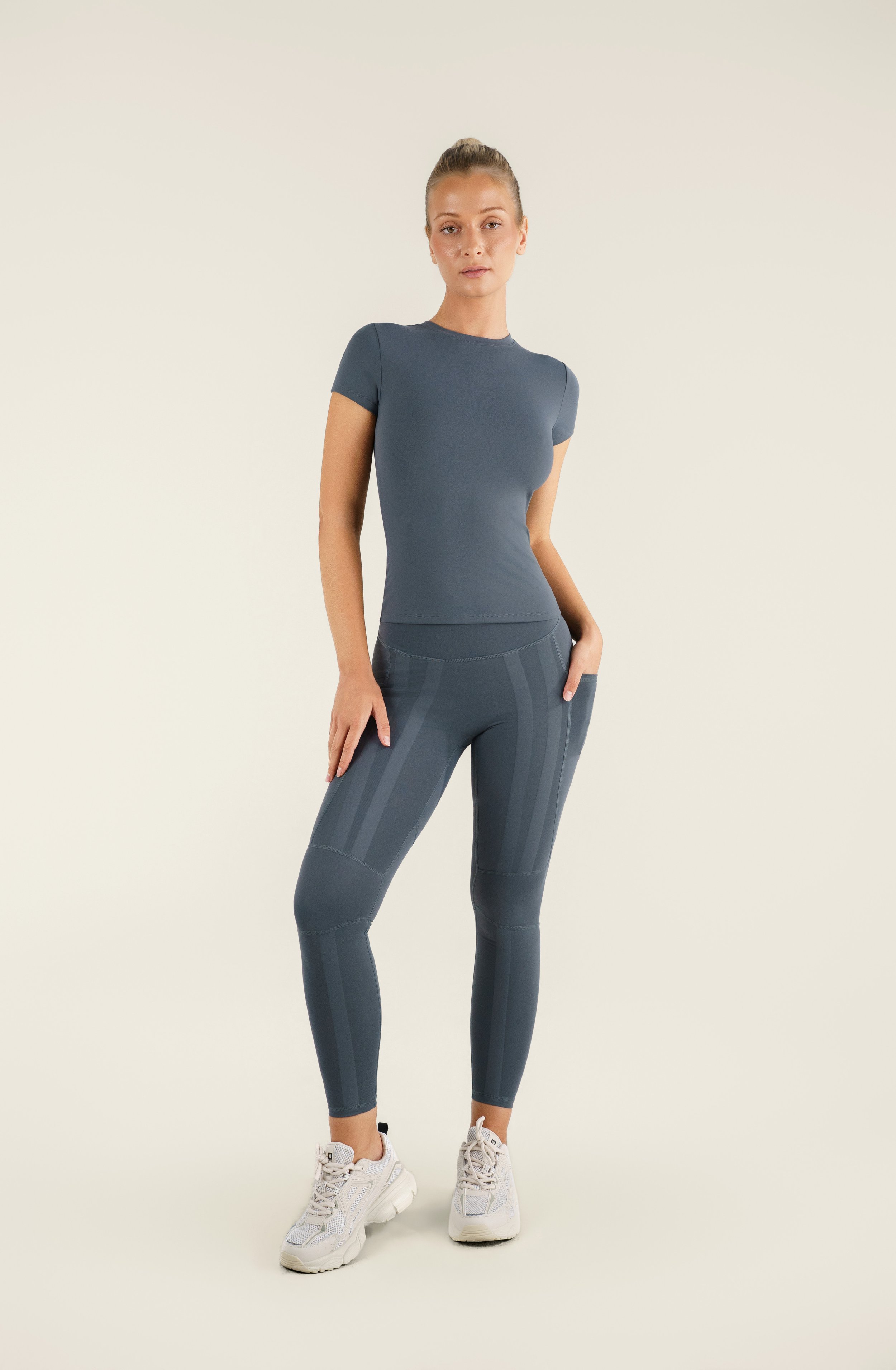 A woman wearing a blue athletic t-shirt and patterned leggings standing against a plain background.