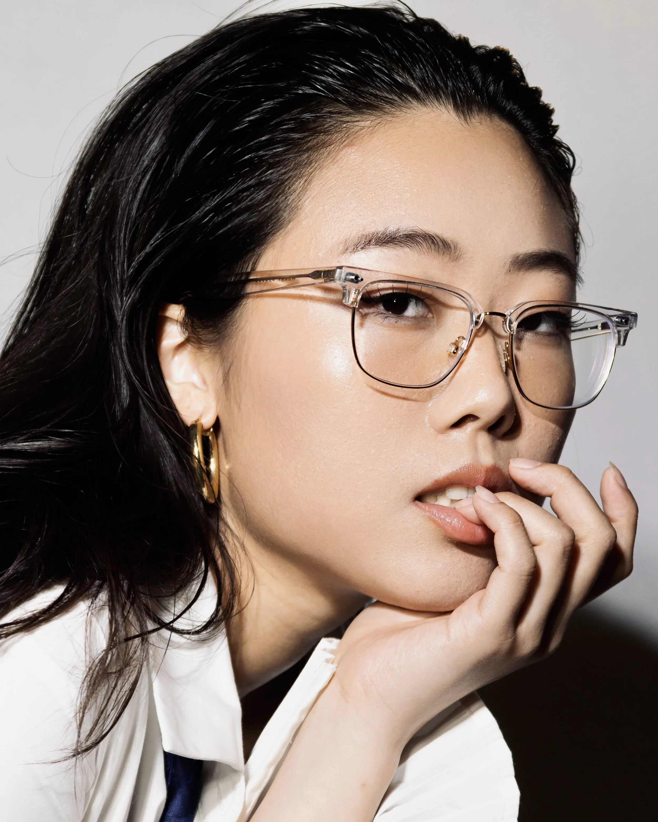 Asian female model with glasses and wet hair biting her lip in editorial and high fashion look.