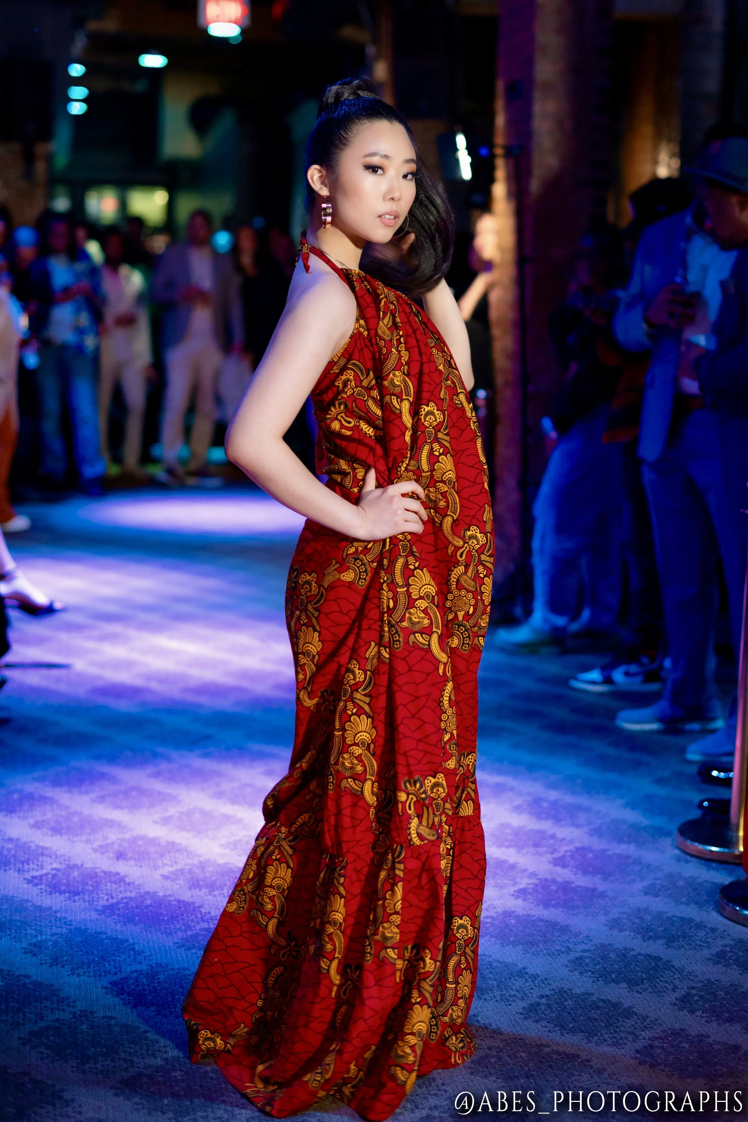 All red floor length dress on model in pose for a fashion show looking over shoulder.