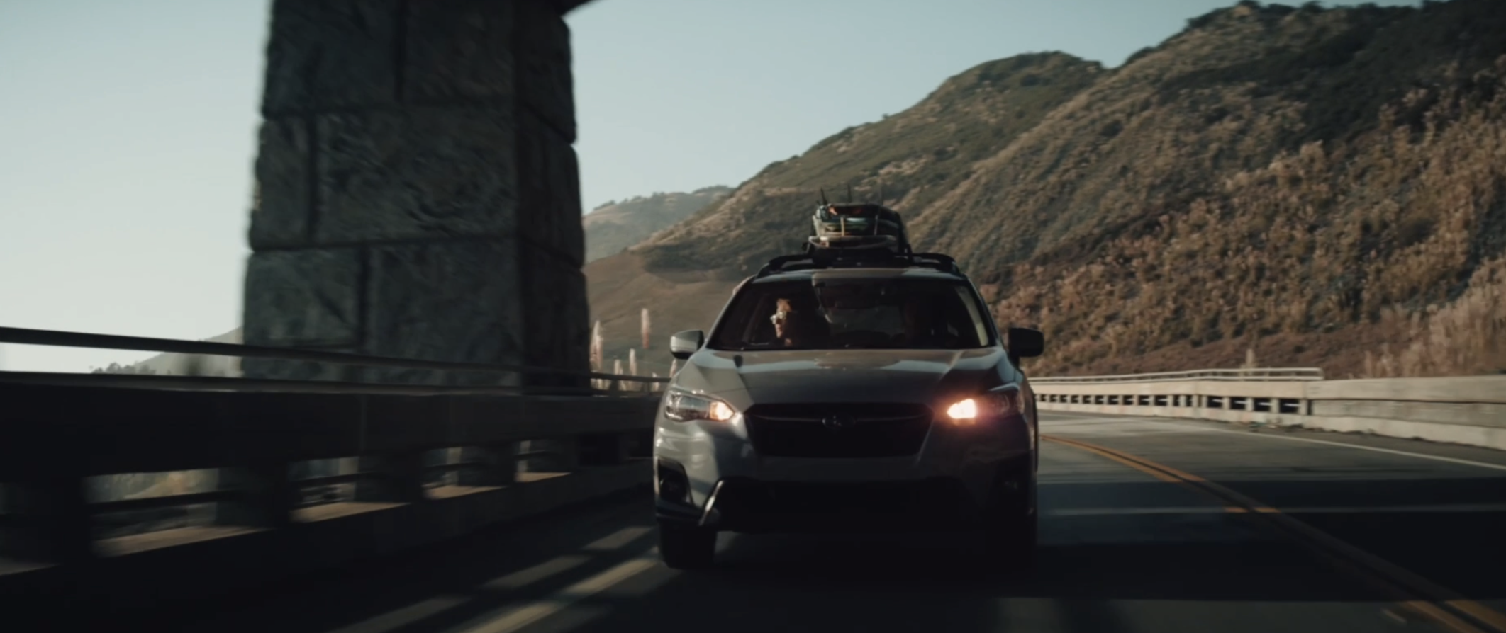 A car driving on a mountain road with traffic, with hills in the background and a large rock formation on the left side.