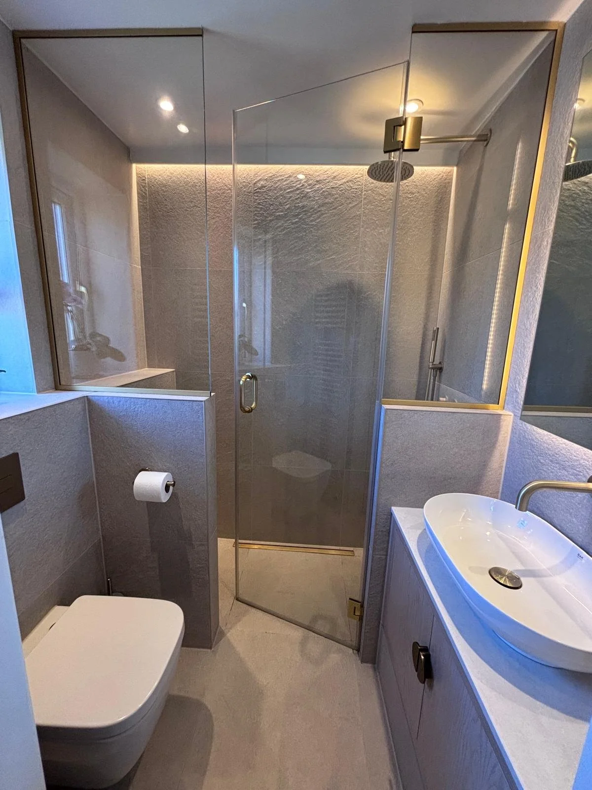 Modern small bathroom with shower enclosure, toilet, and sink, featuring neutral tones and minimalist fixtures.