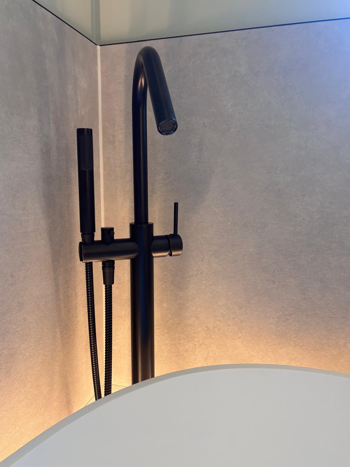 Black kitchen faucet with a high arc spout, two black spray nozzles, and a wall-mounted handle against a textured grey wall.