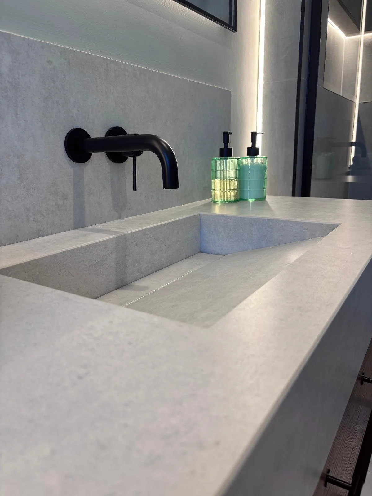 Gray bathroom sink with black faucet and two green soap dispensers on the right side of the sink, against a gray wall with a mirror above.