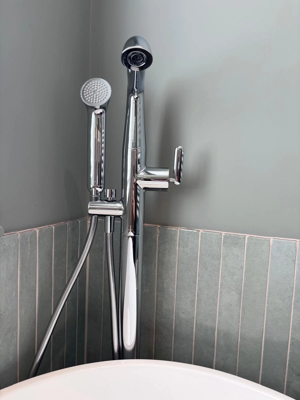 A modern chrome shower faucet with two shower heads, one handheld and one fixed, installed in a bathroom corner with tiled walls.
