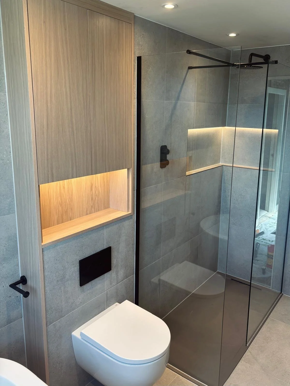 Modern bathroom with a walk-in shower, wooden wall cabinet, white toilet, and gray tiled walls.