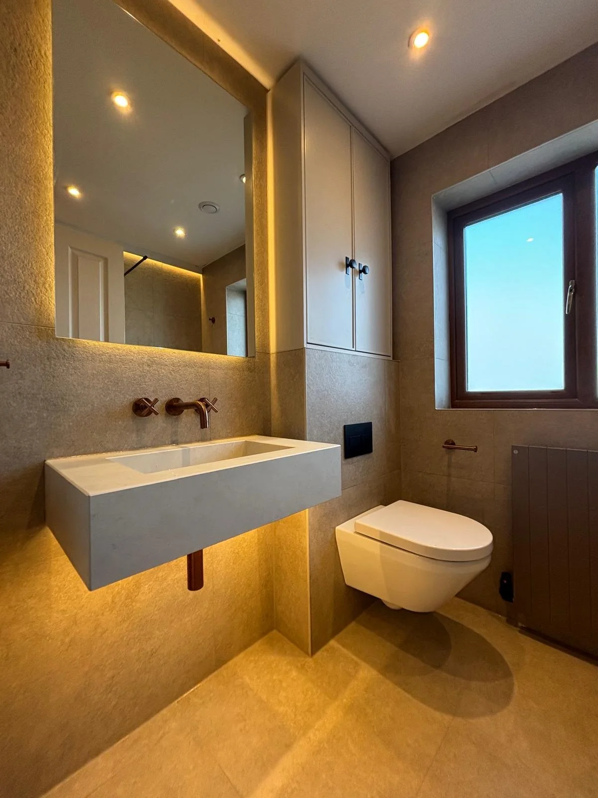 Modern bathroom with a floating sink, mirror, wall-mounted toilet, a window letting in natural light, and built-in cabinets.