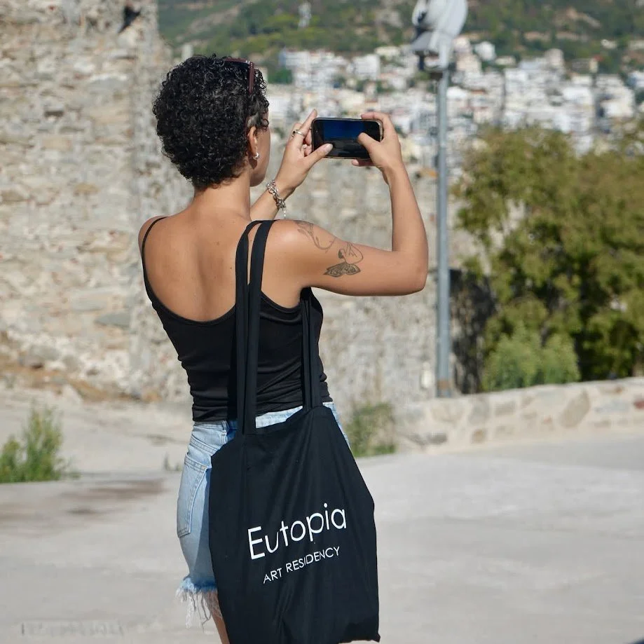 Artist photographing the old town of Kavala, carrying a Eutopia Art Residency tote bag