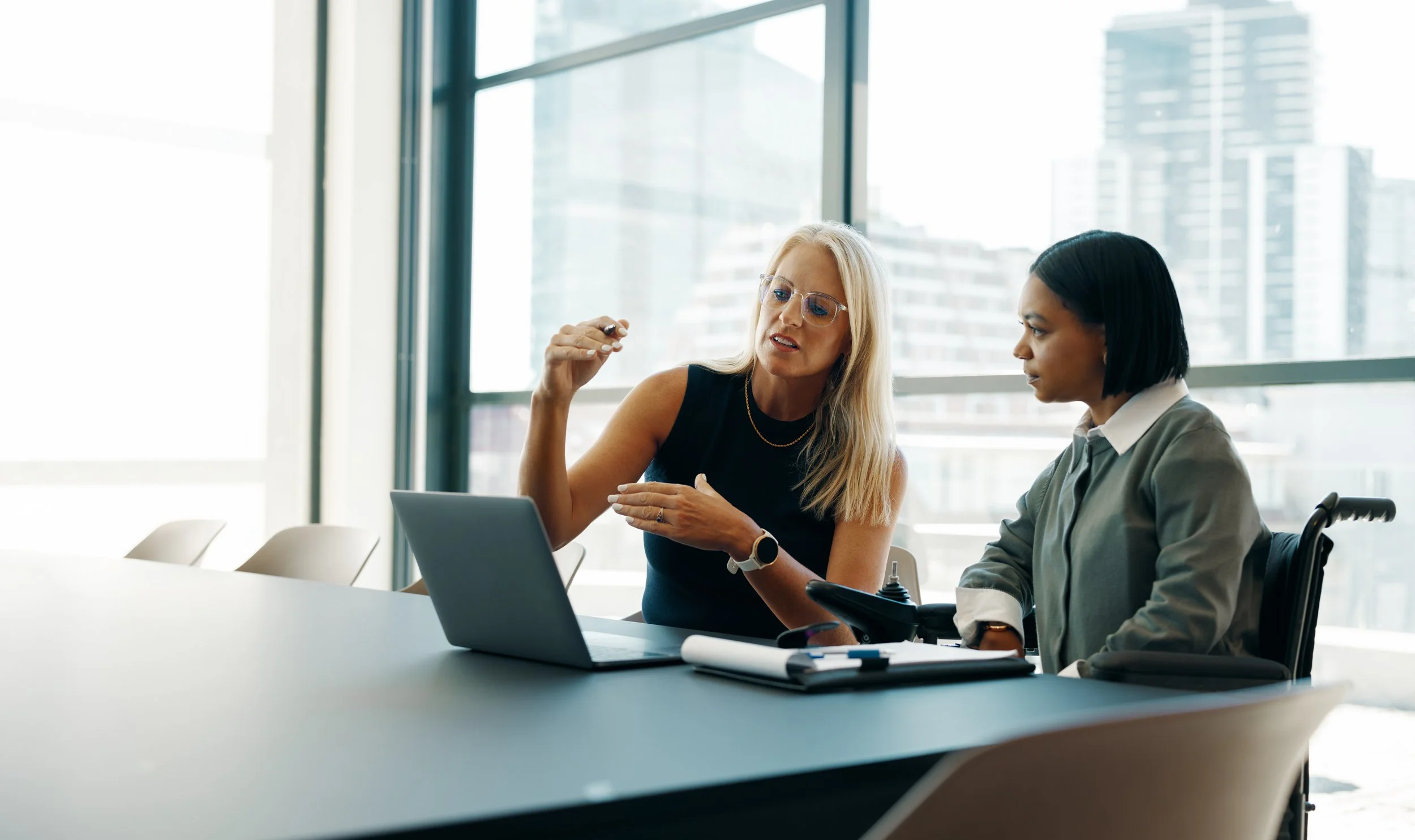 Two professionals collaborating over a laptop during a meeting in a modern office