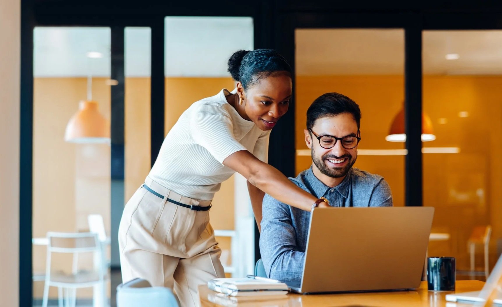 Two coworkers collaborating at a laptop while reviewing work in a modern office
