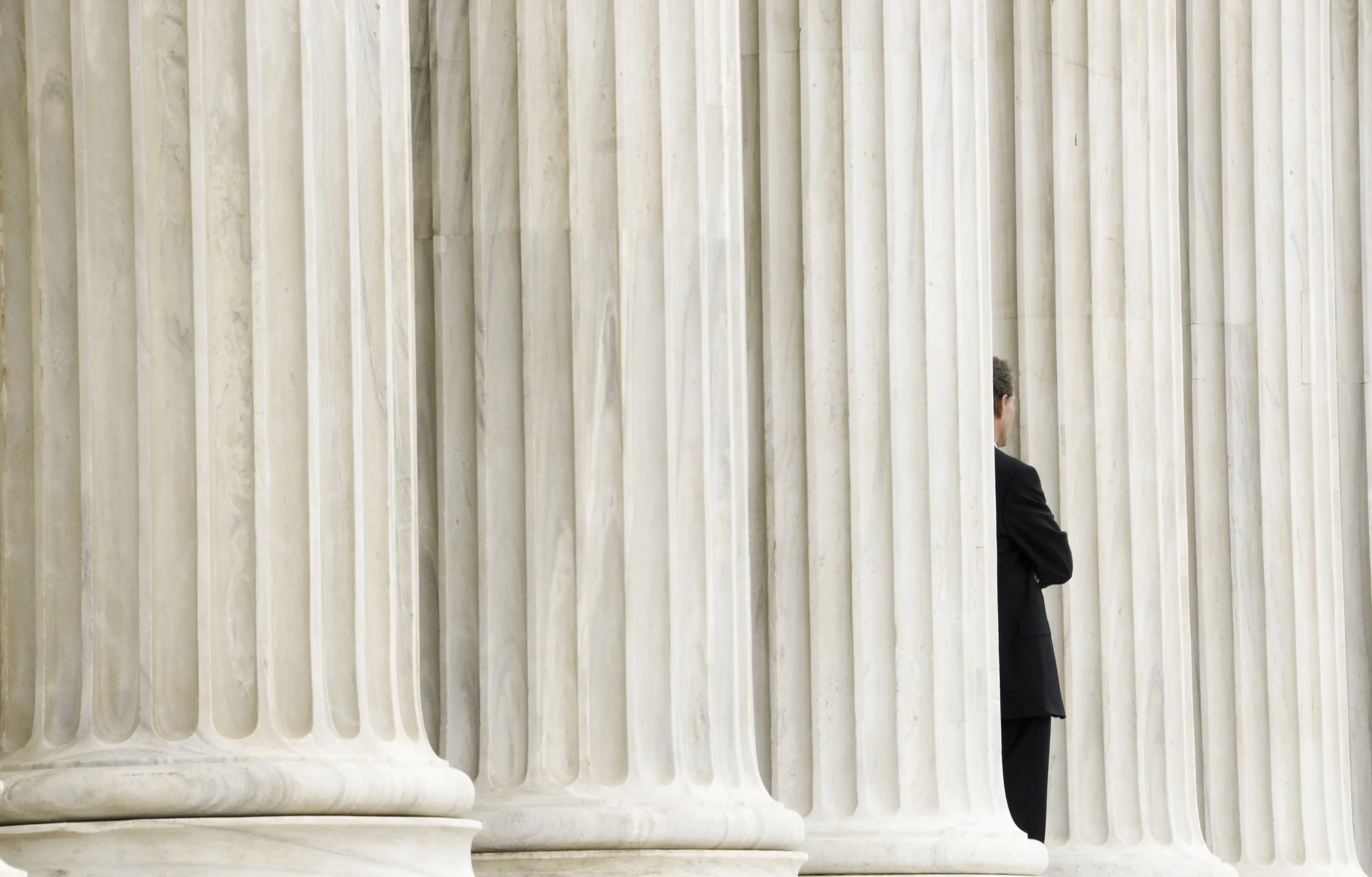 Business professional standing between large stone columns of a government-style building