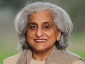 Neelam looks to camera smiling in neutral clothing with her grey hair brushed back around her shoulders