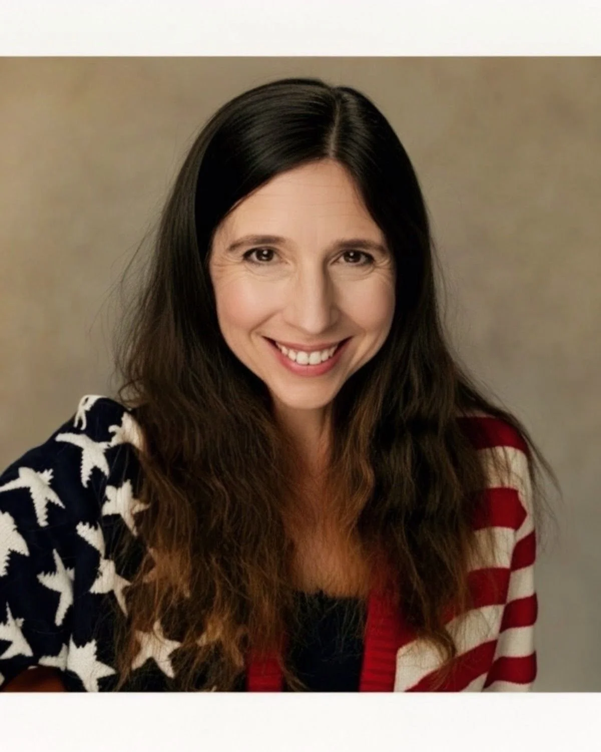 A woman with long dark brown hair smiling at the camera, wearing a jacket with American flag pattern.