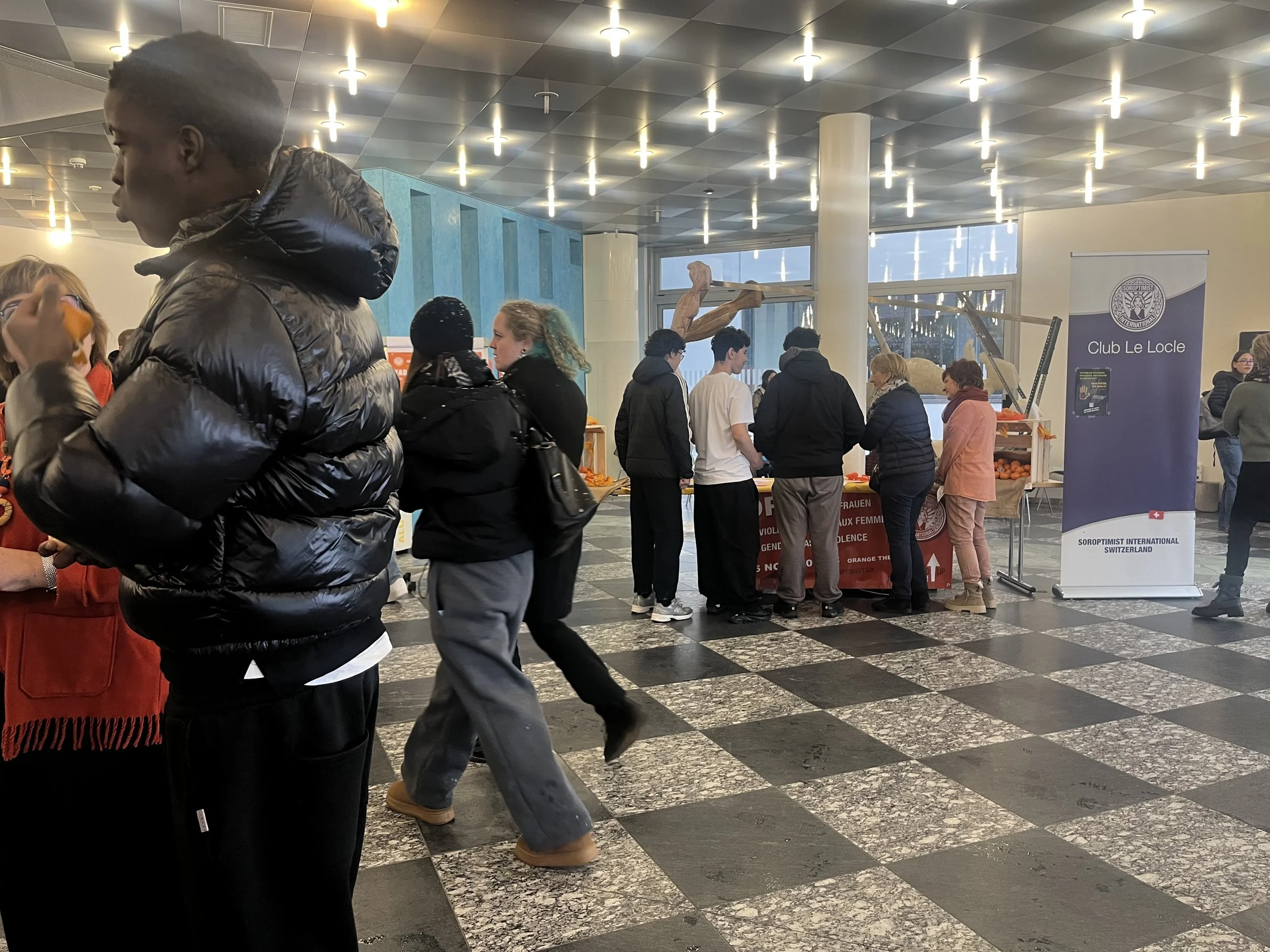 Groupe de personnes échangeant des produits dans un hall d'aéroport, avec un stand initié par un club de Suisse.