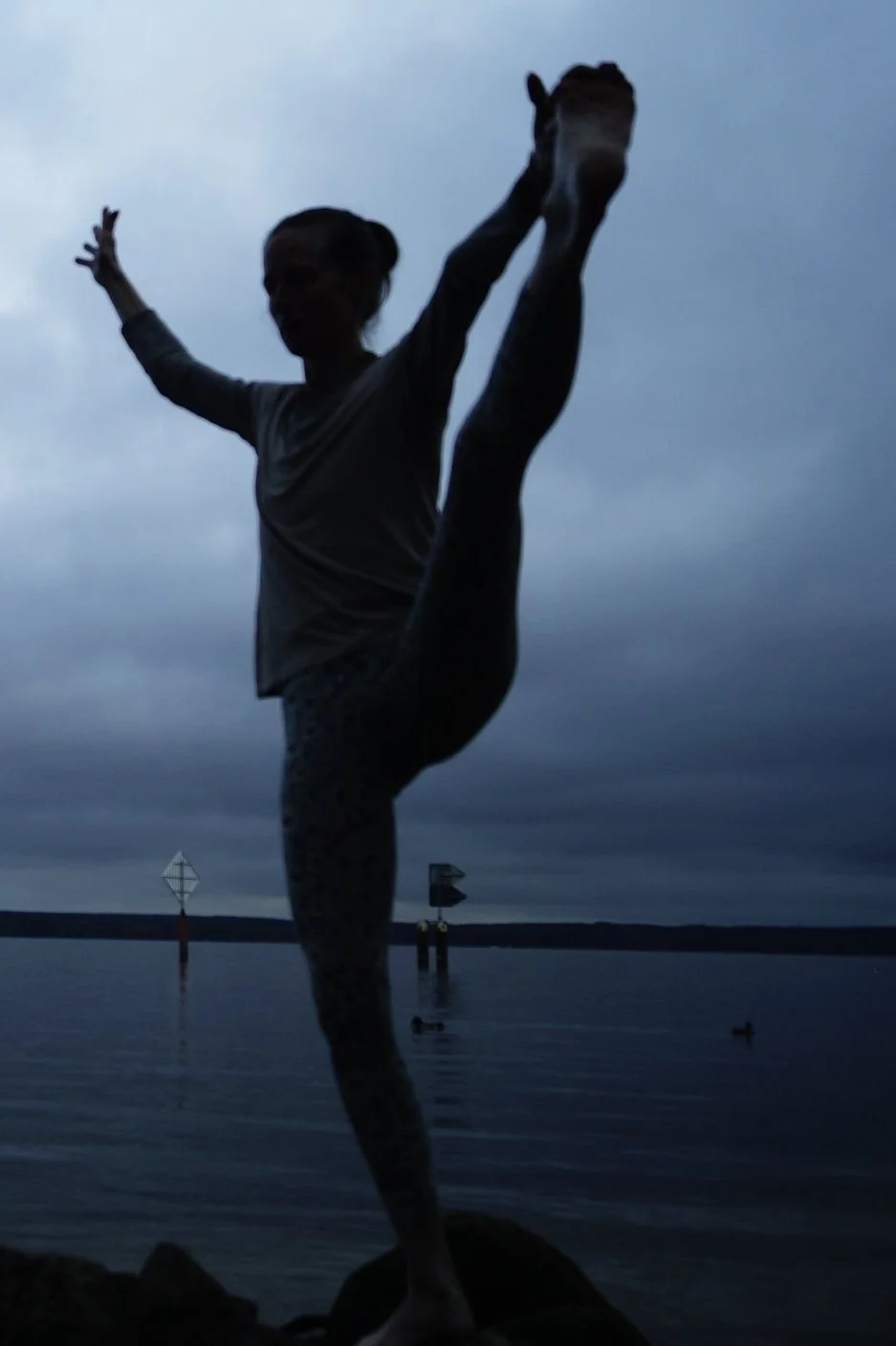 Frau vor einem See in Utthita Padangushthasana (Sanskrit उत्थितपादाङ्गुष्ठासन utthita-pādāṅguṣṭhāsana, deutsch Aufgerichtete Großzehenstellung), ein Asana (Stellung) aus Yoga (Yogaposition). Variation von Padangushthasana, Utthita - aufgestanden