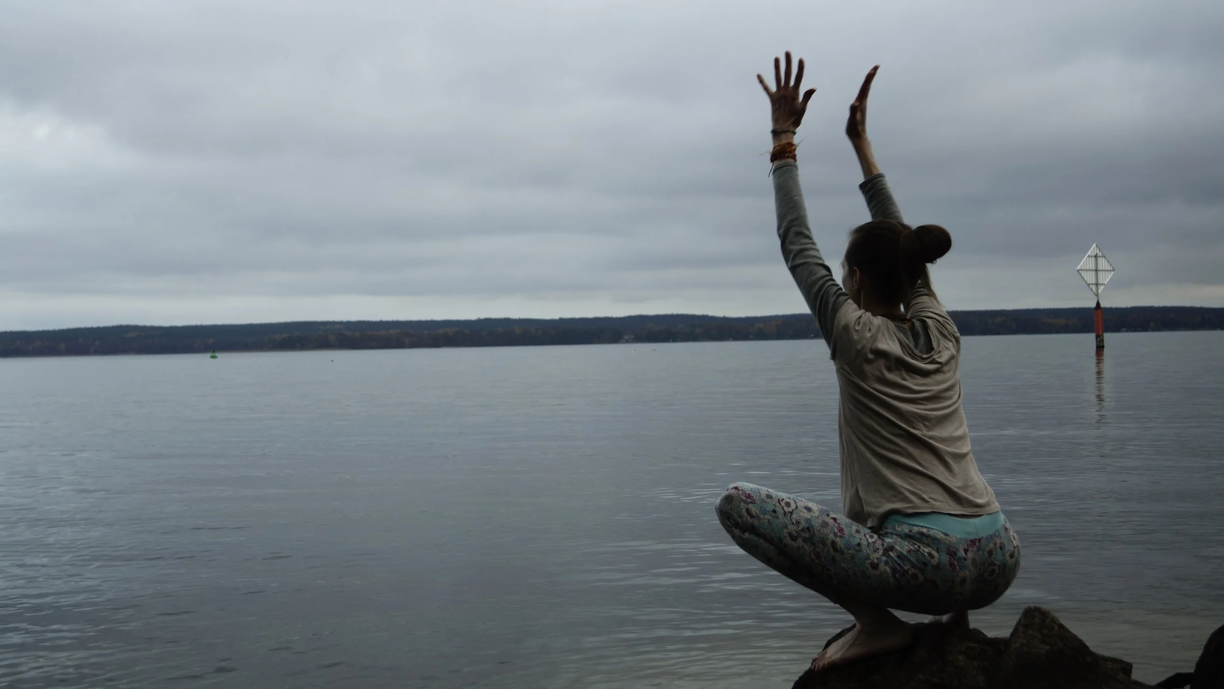 Frau (Karina Gaurangi Schmuck) am Wasser in tiefer Hocke mit gestreckten Armen über dem Kopf