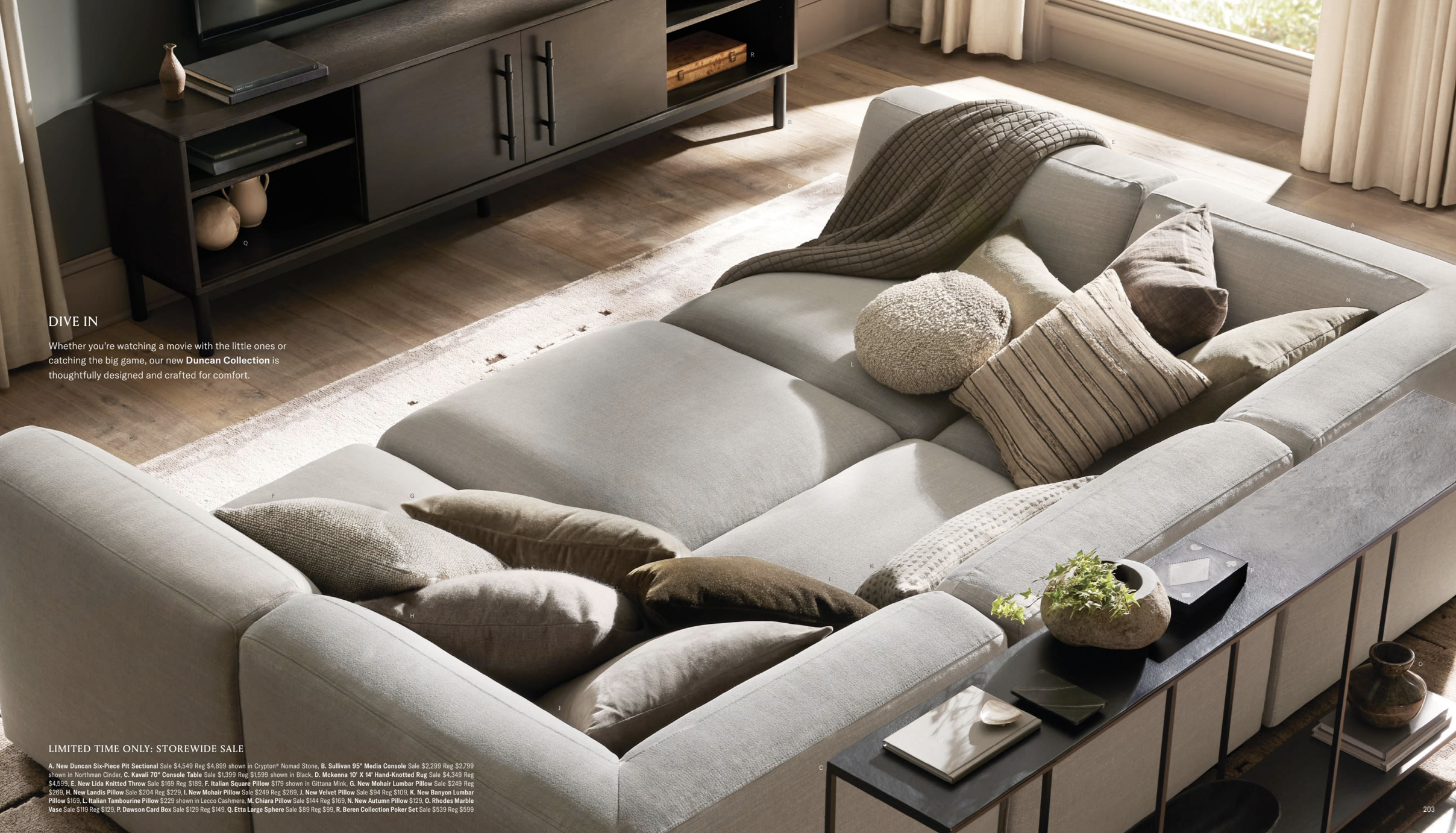 Arhaus 2024 Fall Catalog -- photo shows an above view of a large, modular couch. cozy pillows are tossed on top, alongside a blanket which hangs over the arm of the couch. a diffused light shines in from the window.