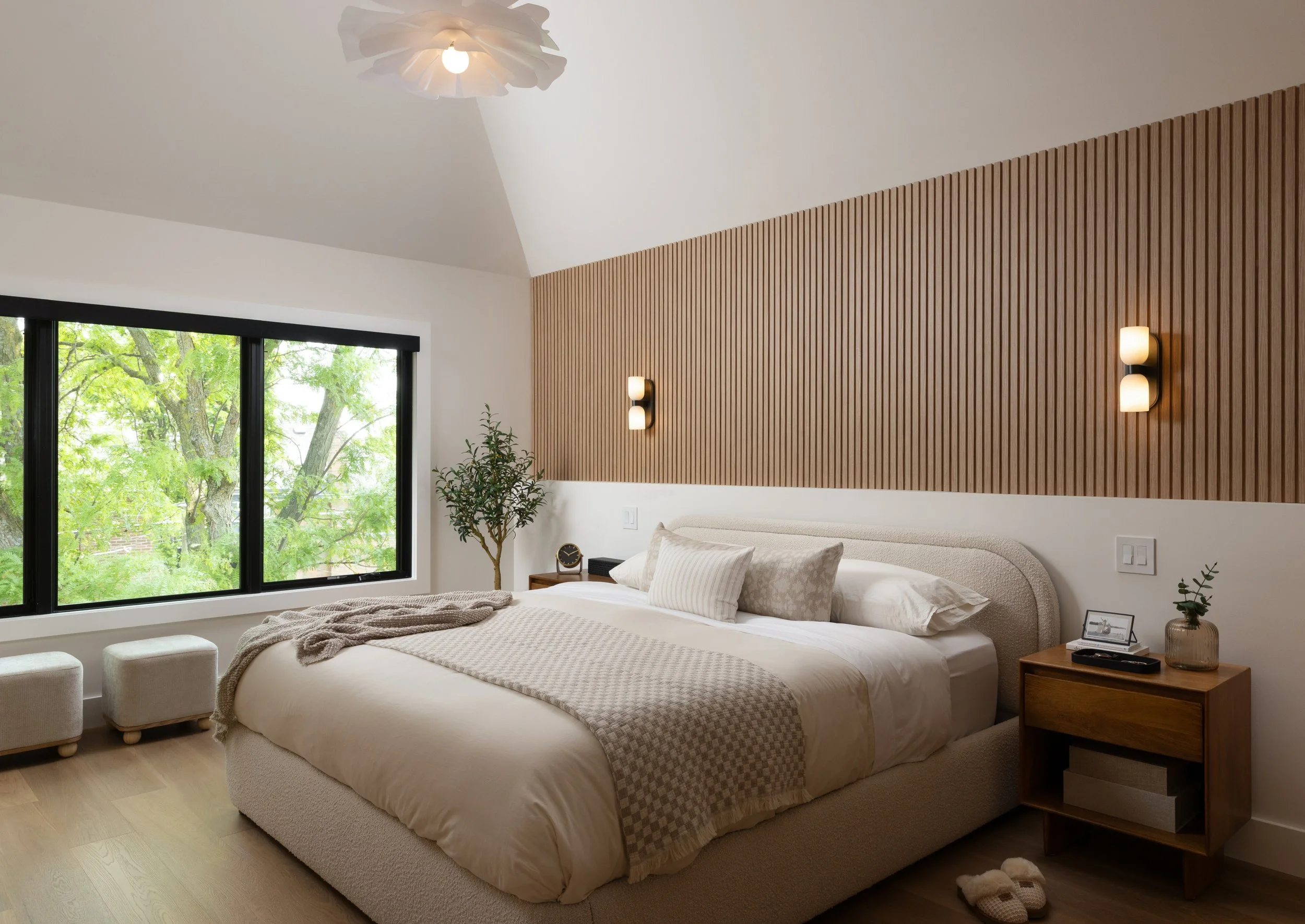 Bright modern bedroom with decorative custom millwork above the modern bed with upholstered headboard, floating side table and modern overhead light fixture and small wall sconce