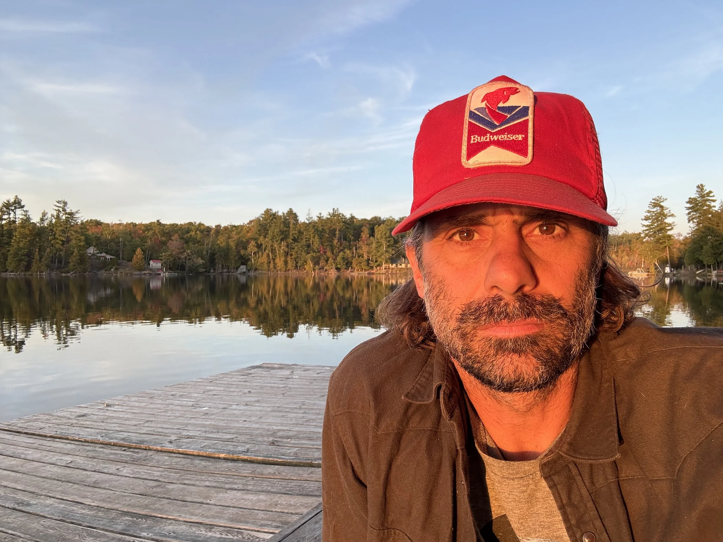 Man with long hair and beard wearing a hoodie with 'de BLOIS BUILT' logo, smiling, in black and white.