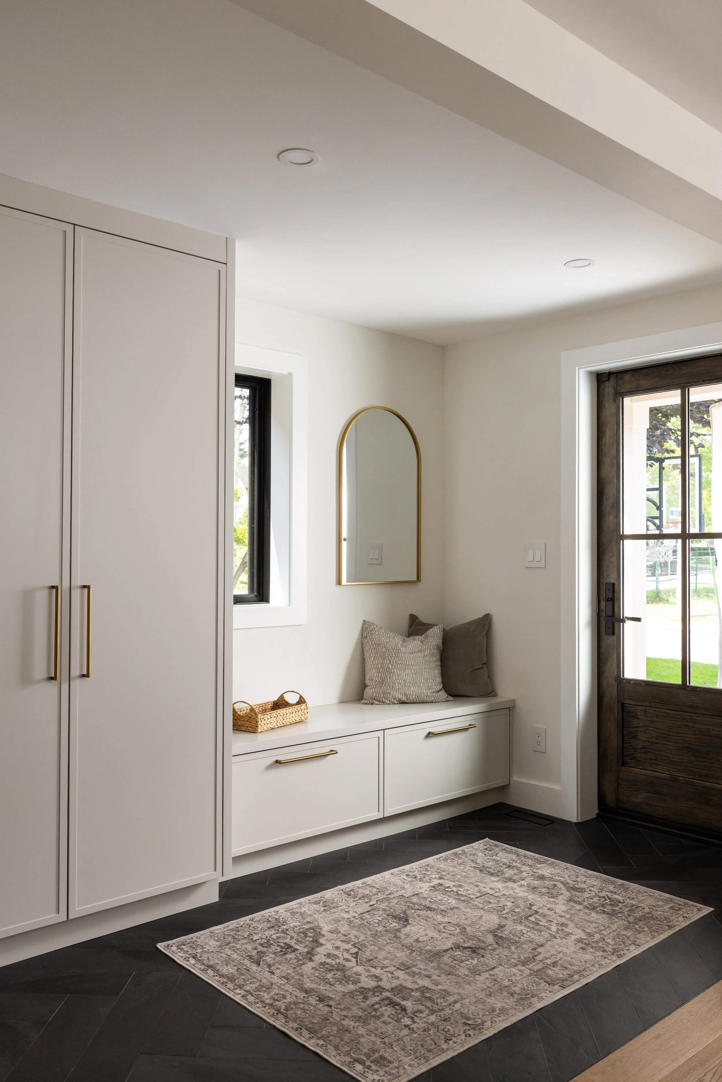 Relaxed entryway with bench and custom cabinetry below adjacent to a large wooden front door with large glass panes