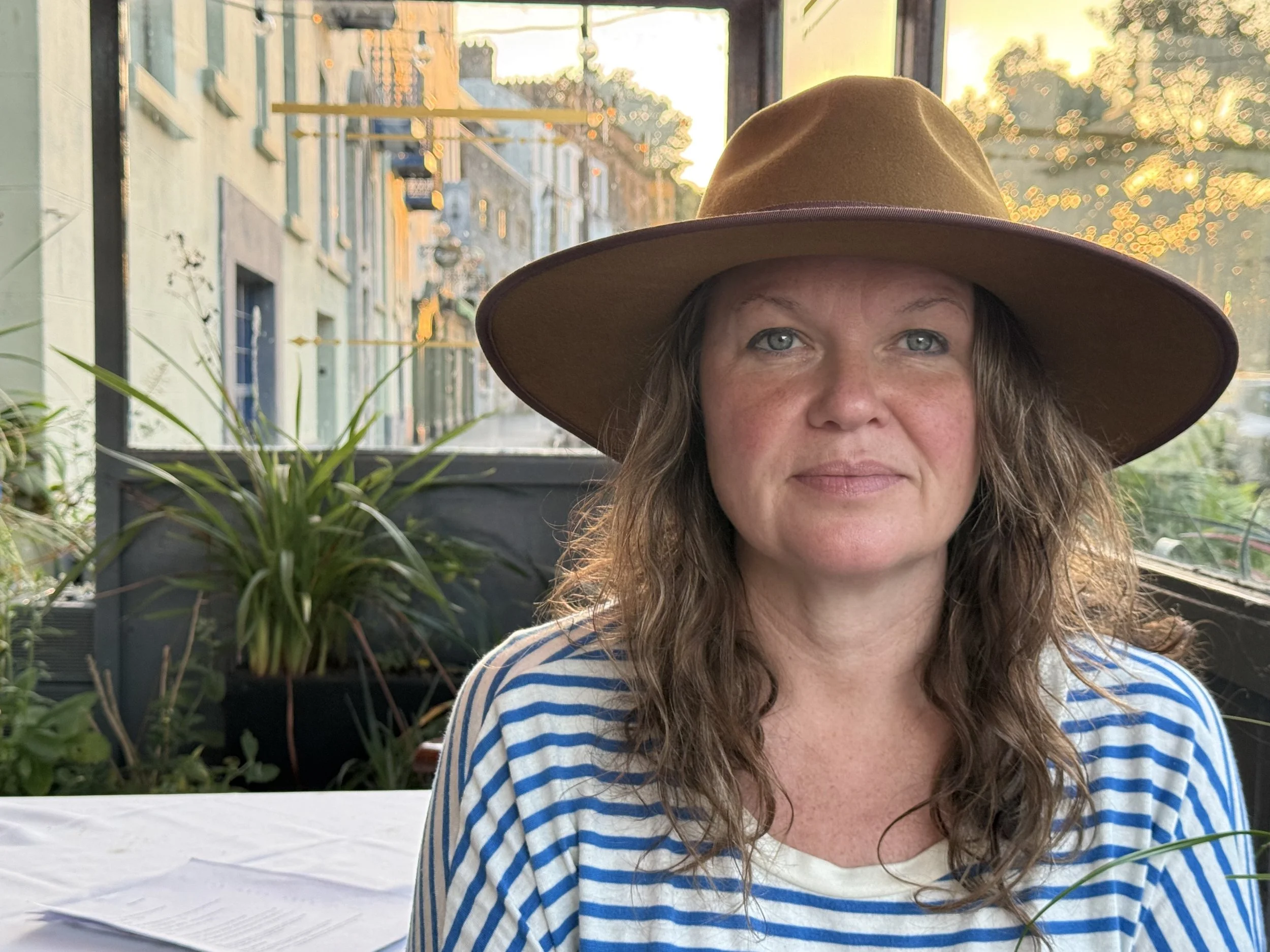 Colour portrait of a woman with shoulder-length wavy hair, wearing a tan hat, smiling slightly