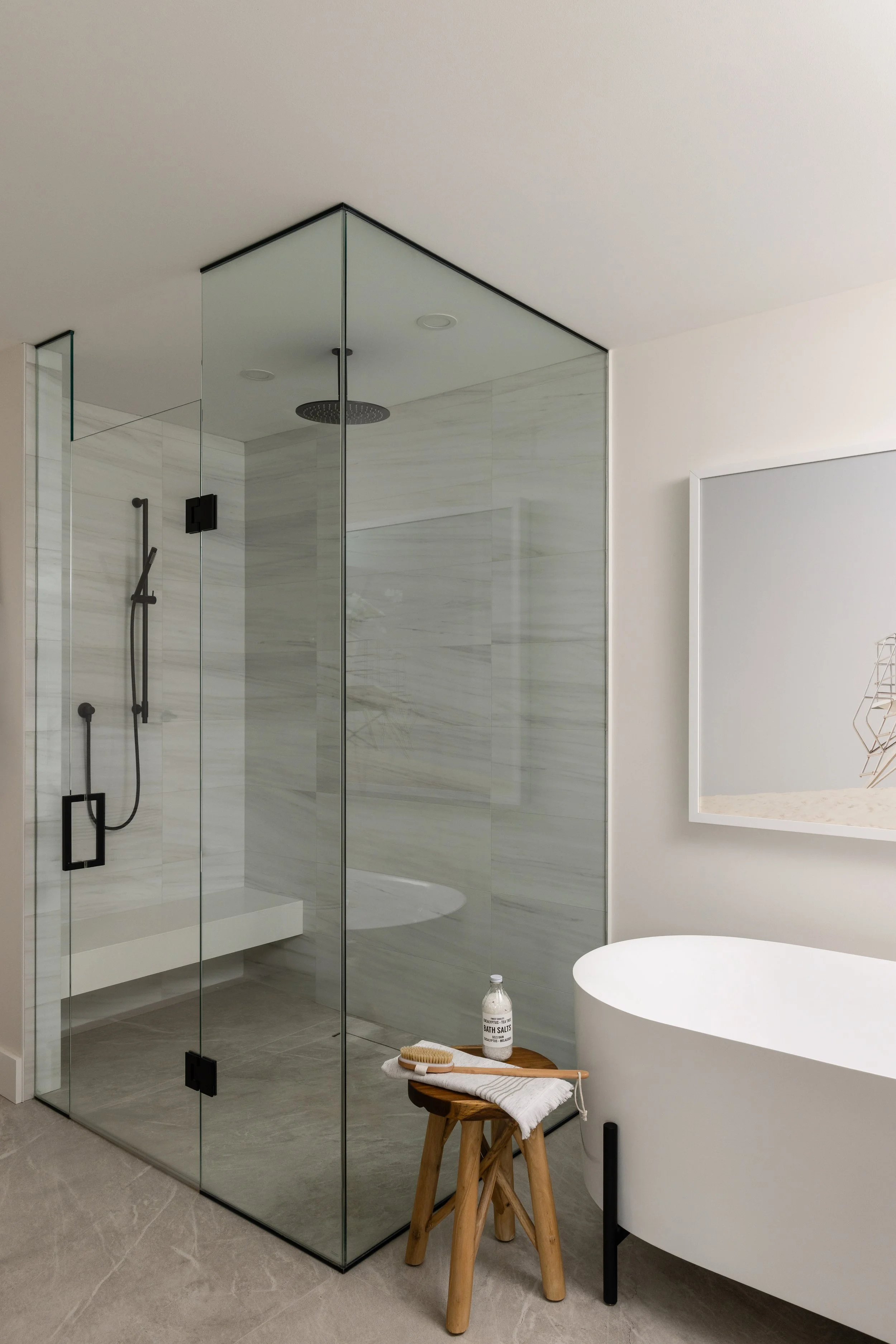 A large custom frameless glass shower with rain showerhead, marble walls, and bench next to a deep soaker tub