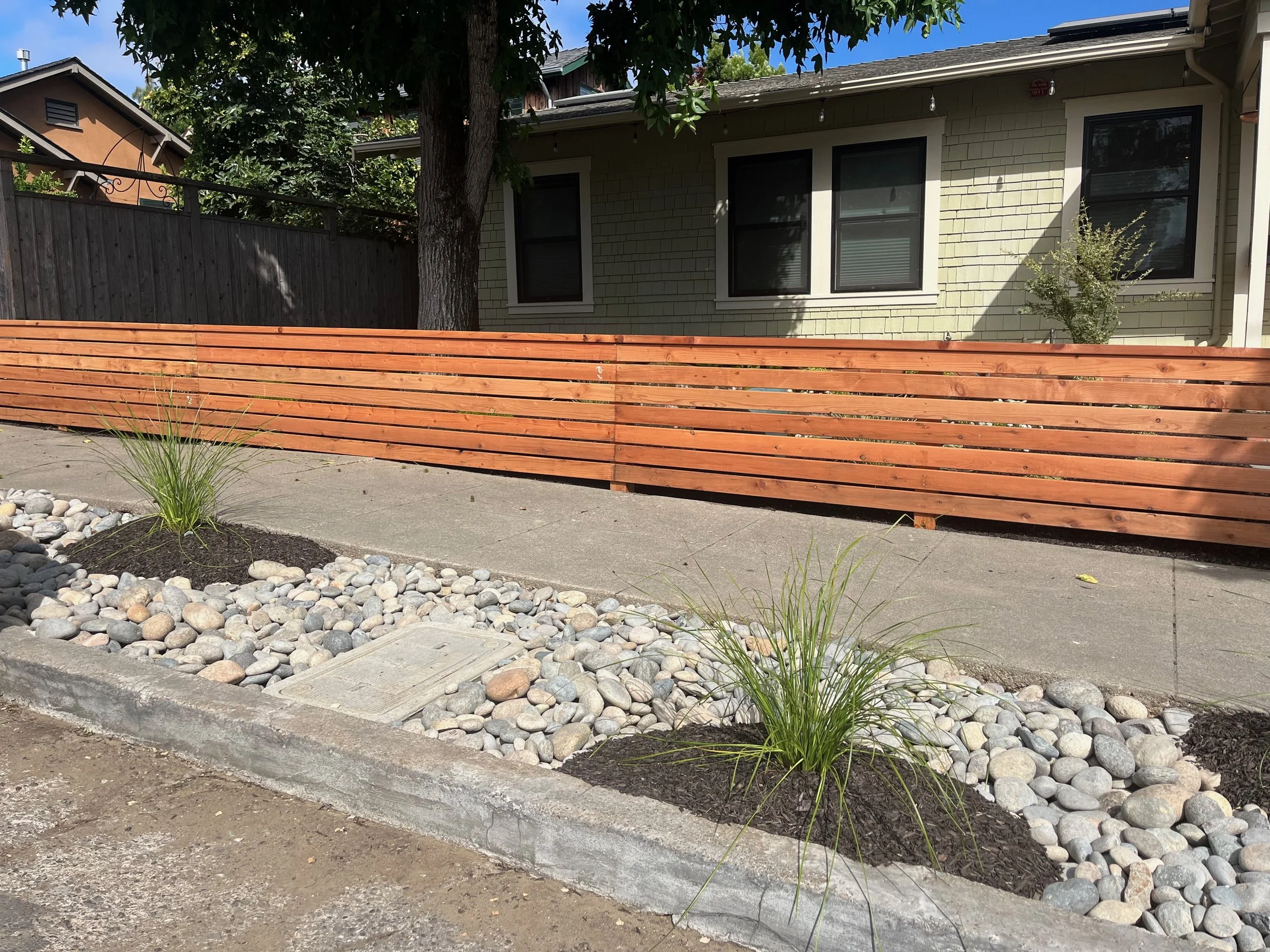 Redwood Horizontal fence and median strip with cobbles and ornamental grasses.