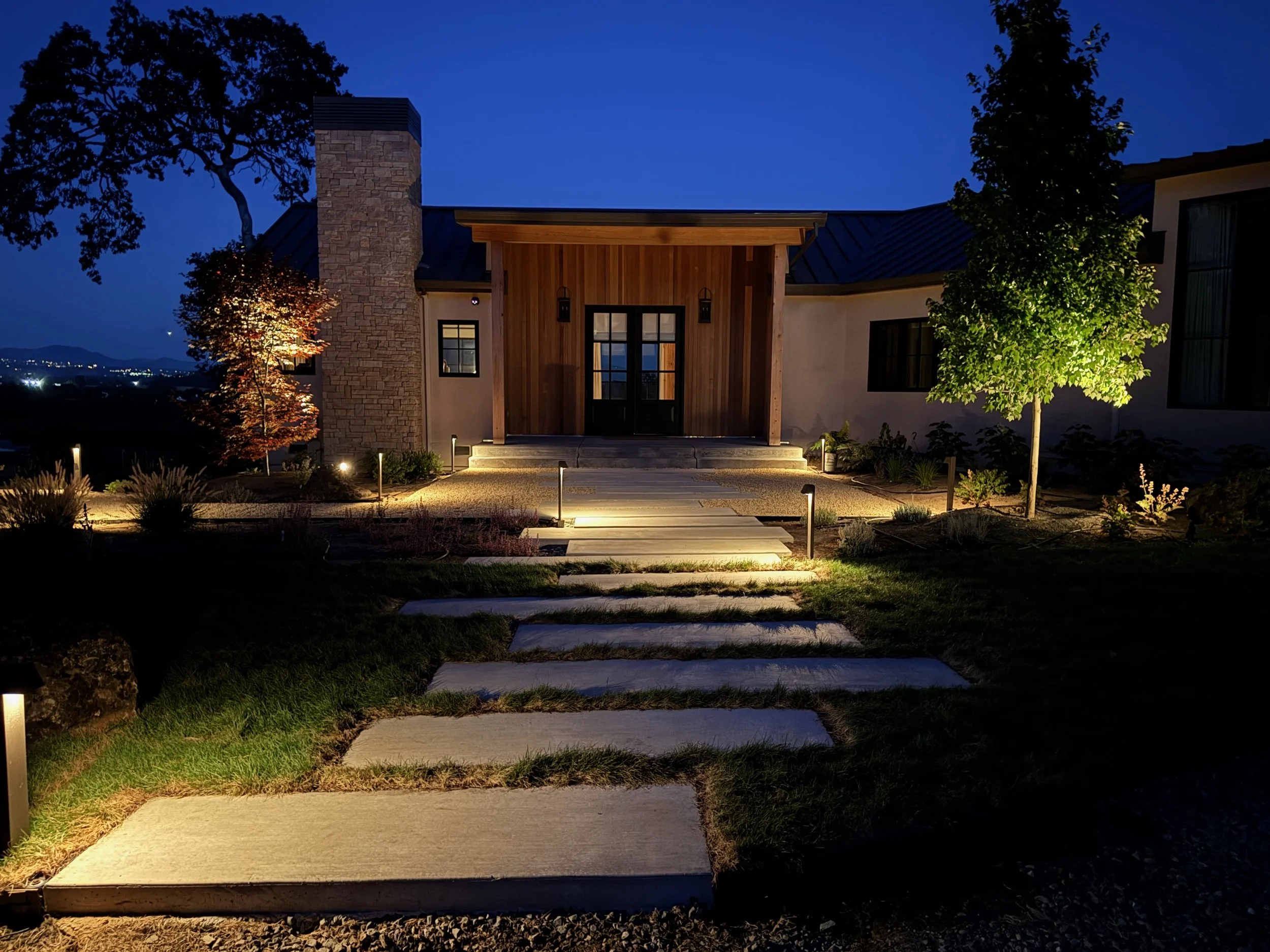 Outdoor lighting along modern walkway with uplight into trees and path lights along a walkway and fescue grass surrounding.