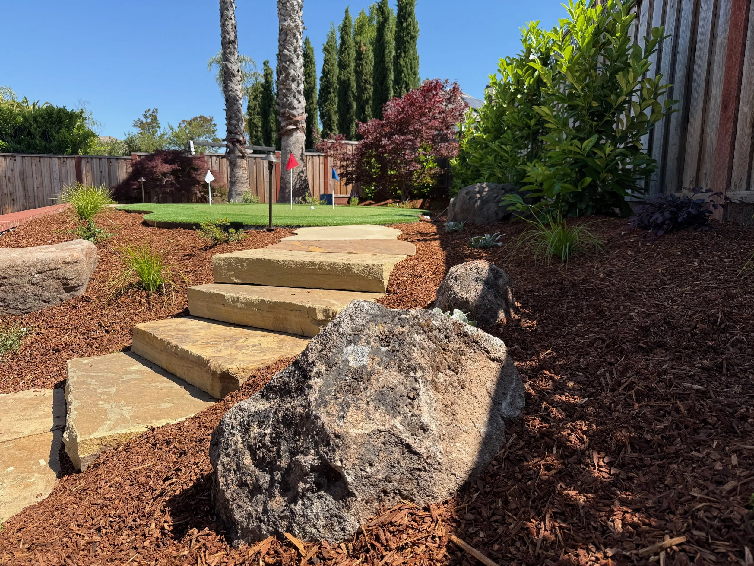 Sonoma fieldstone boulder in landscape with stone steps and putting green in the background.