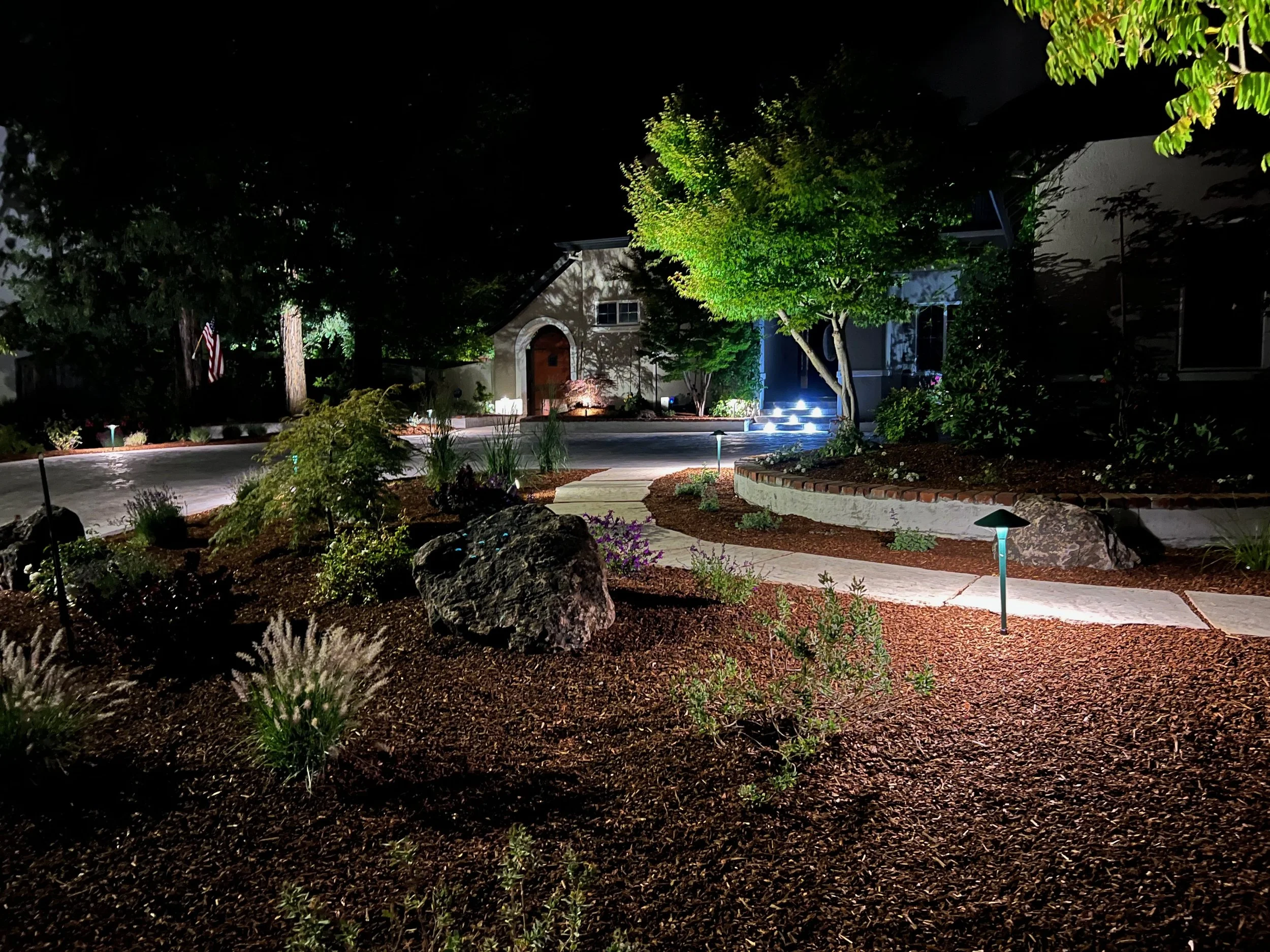 Front yard landscape with boulders, ornamental grasses, and outdoor lighting along a flagstone pathway.