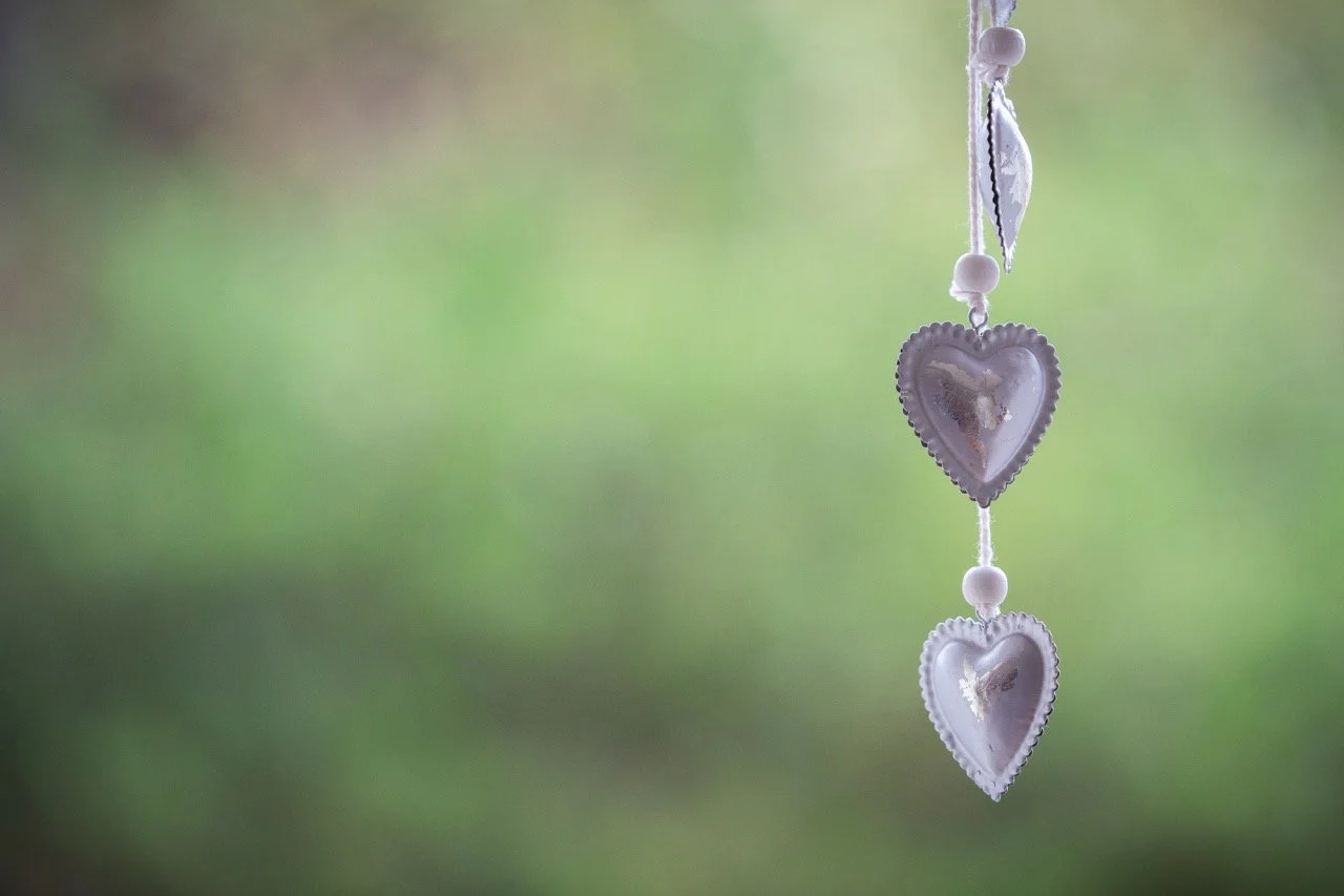 A hanging decoration with three silver heart-shaped ornaments connected by a string, with a blurred green background.