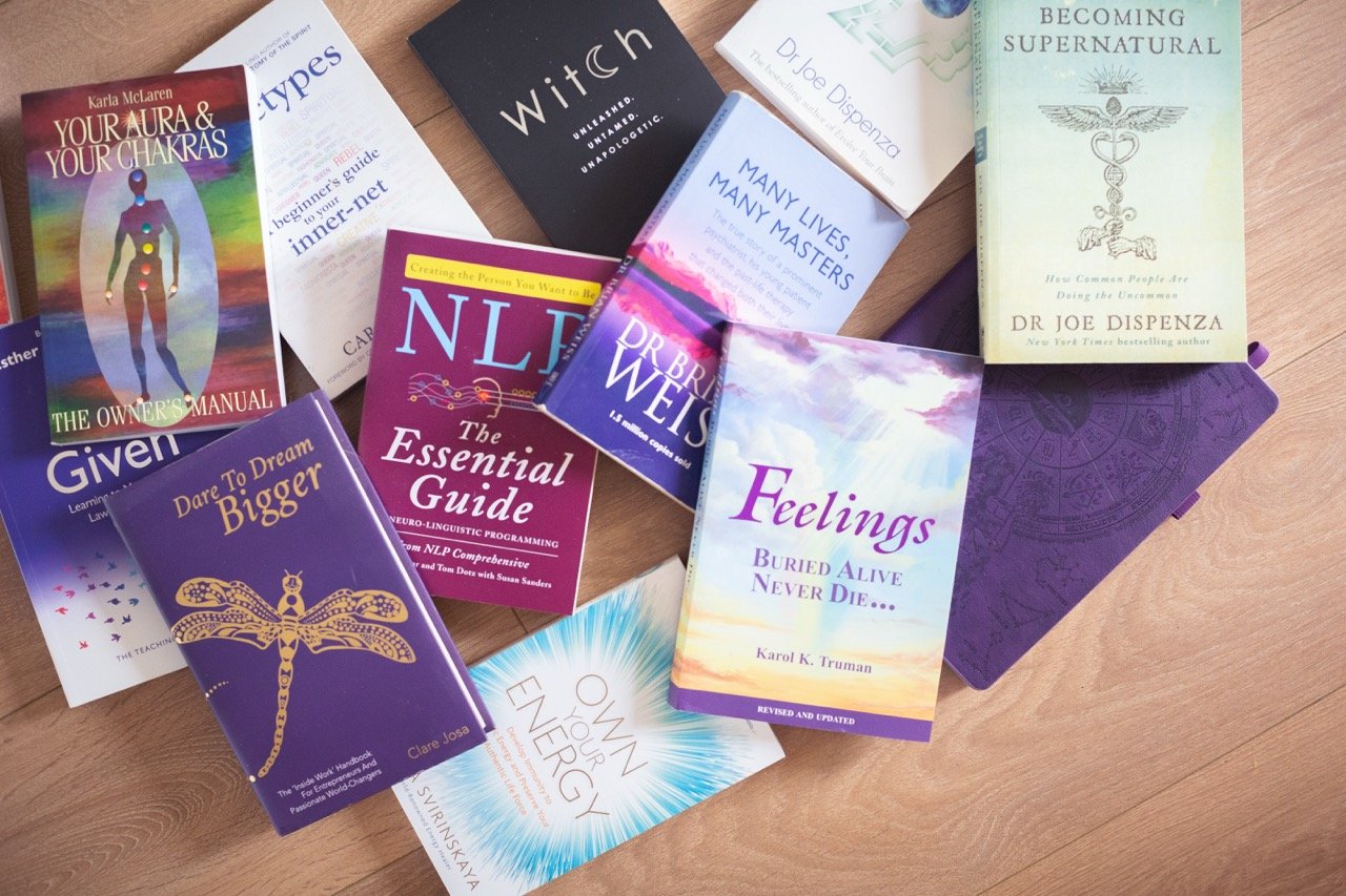 A collection of books on spirituality, self-help, and energy readings arranged on a wooden surface, with some books overlapping and open.