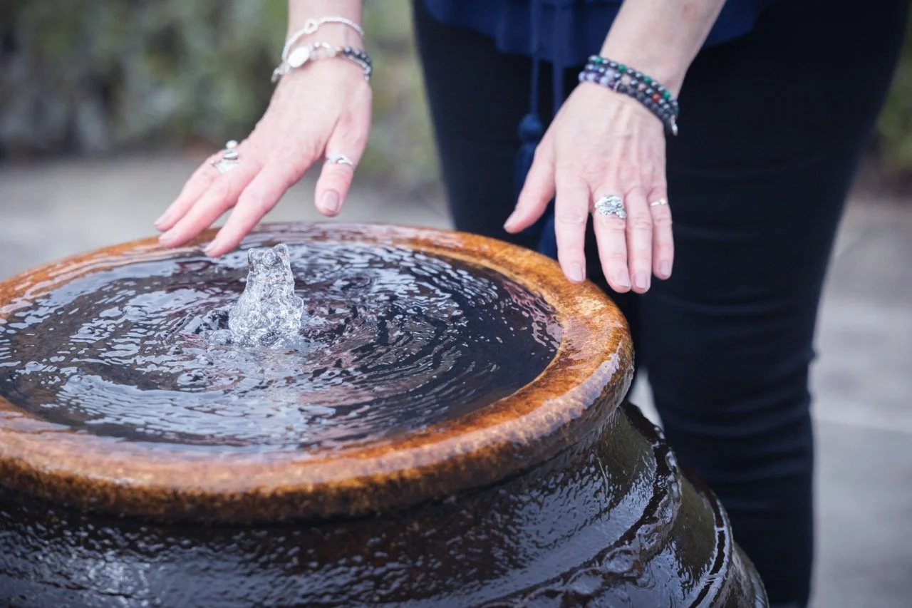 Person touching water in a small fountain with a stone sculpture in the center.
