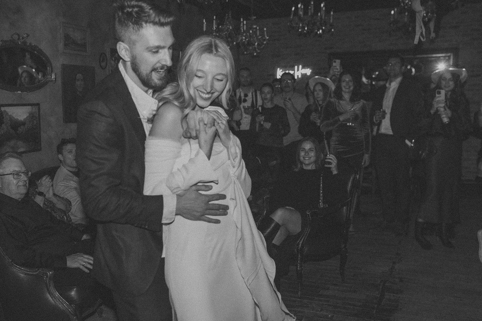 Black and white photo of a couple dancing while people watch and take photos at a party.
